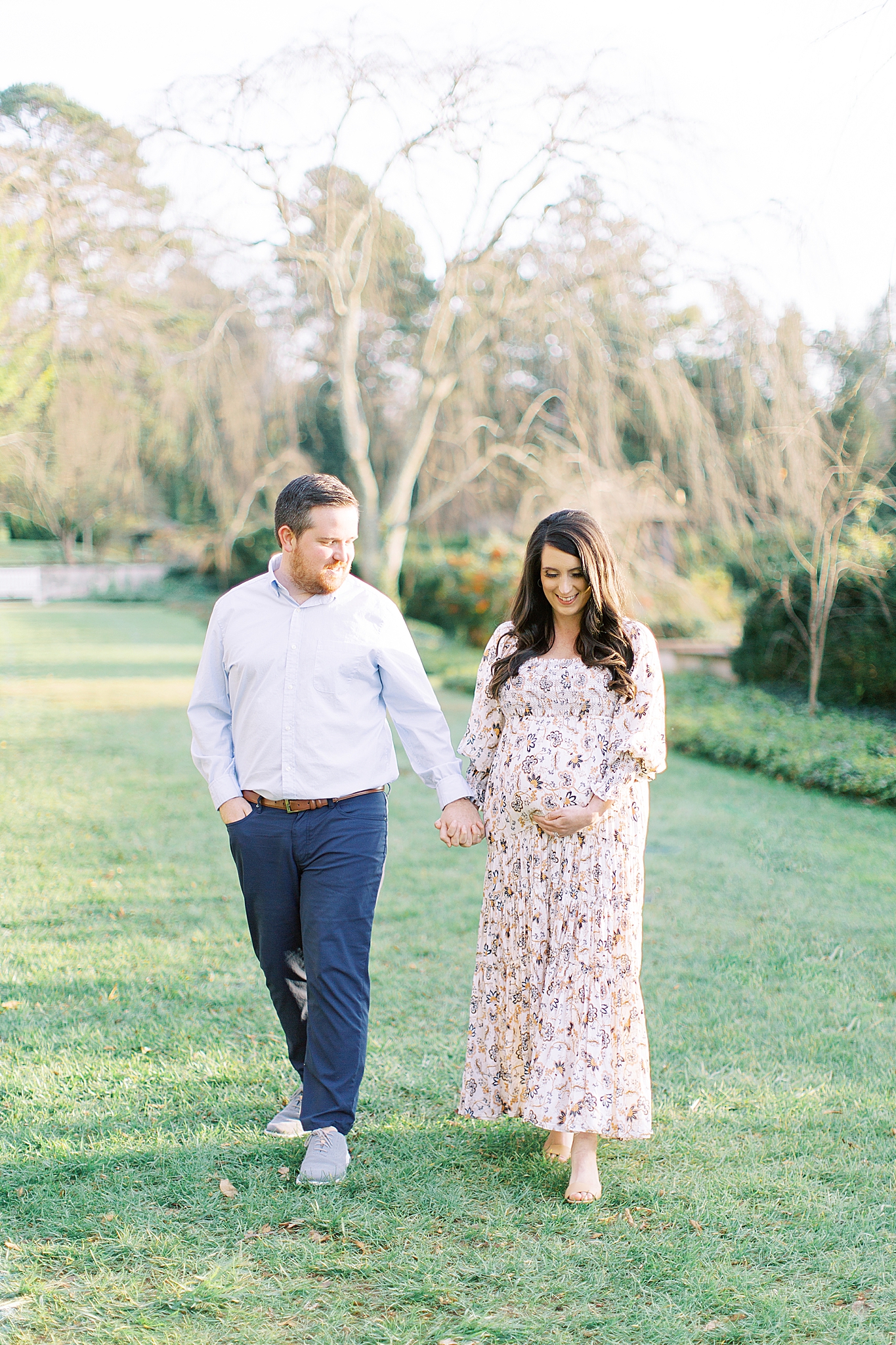expecting couple holds hands walking through Reynolda Village gardens