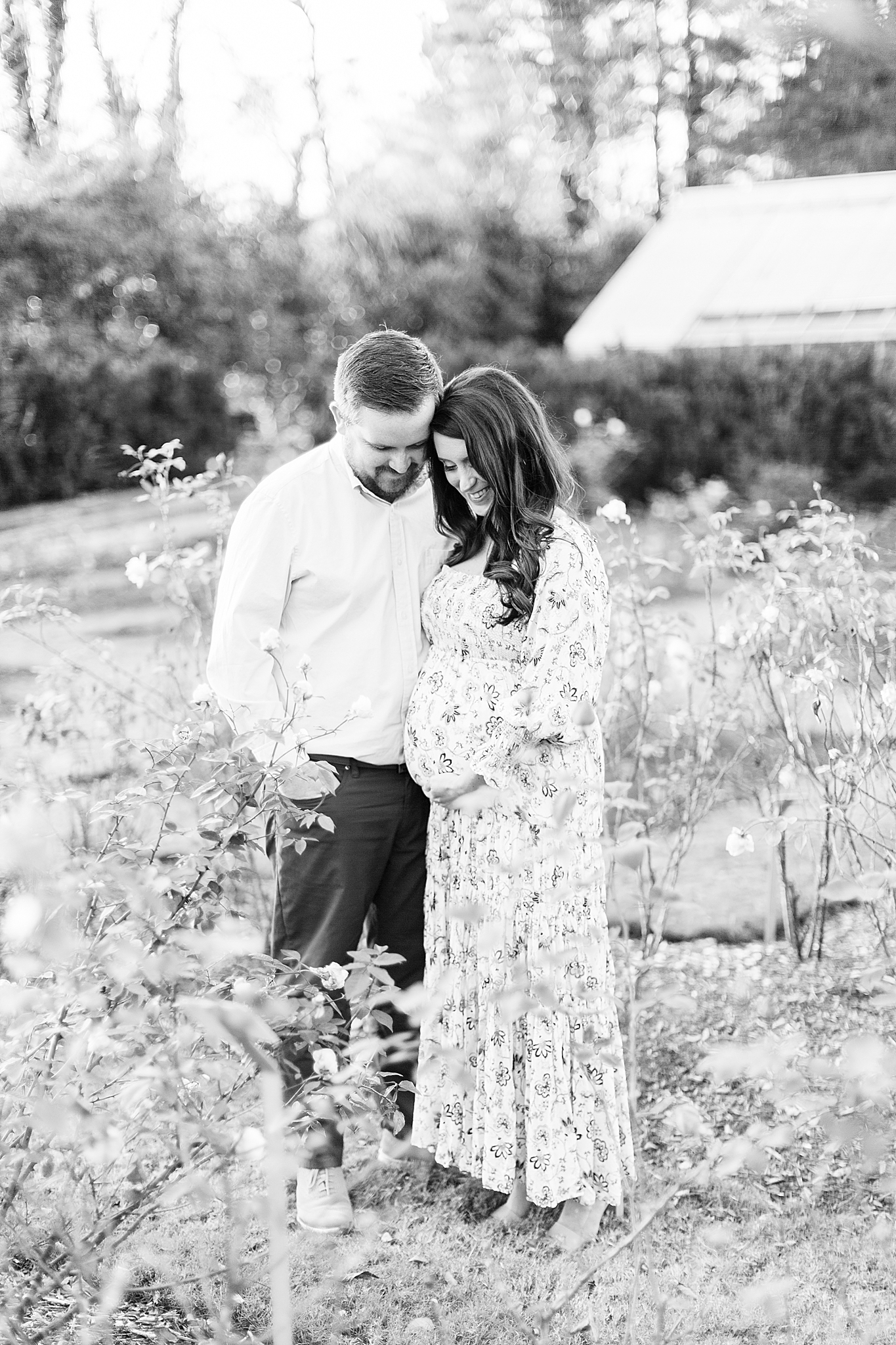 husband and wife look down at baby belly during maternity portraits in Reynolda Village