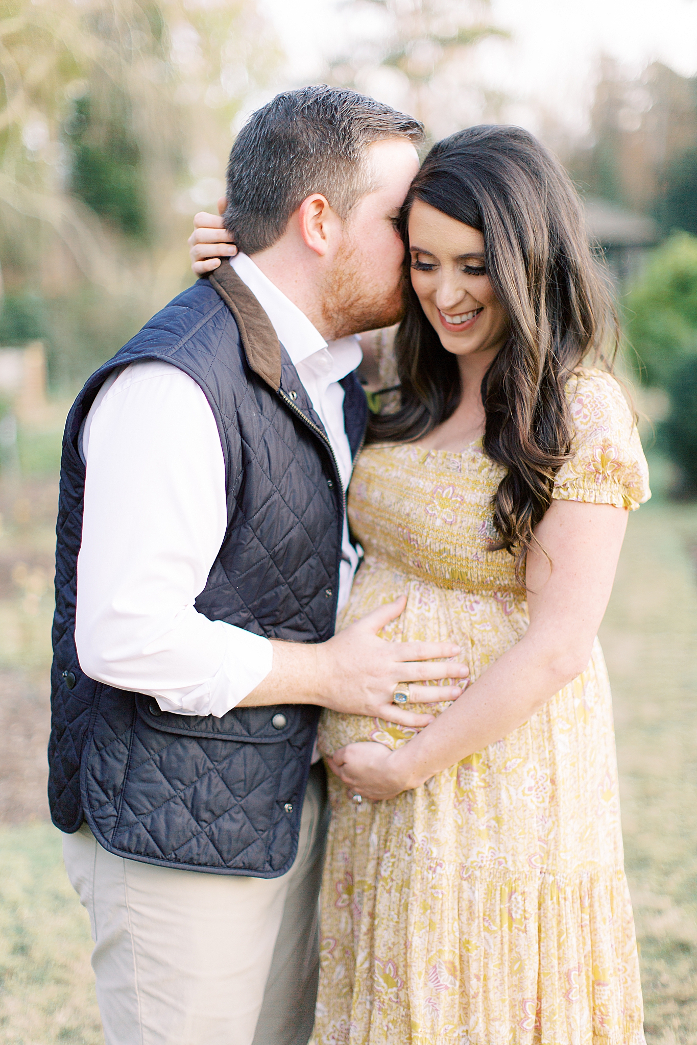 husband kisses wife's cheek and holds baby belly