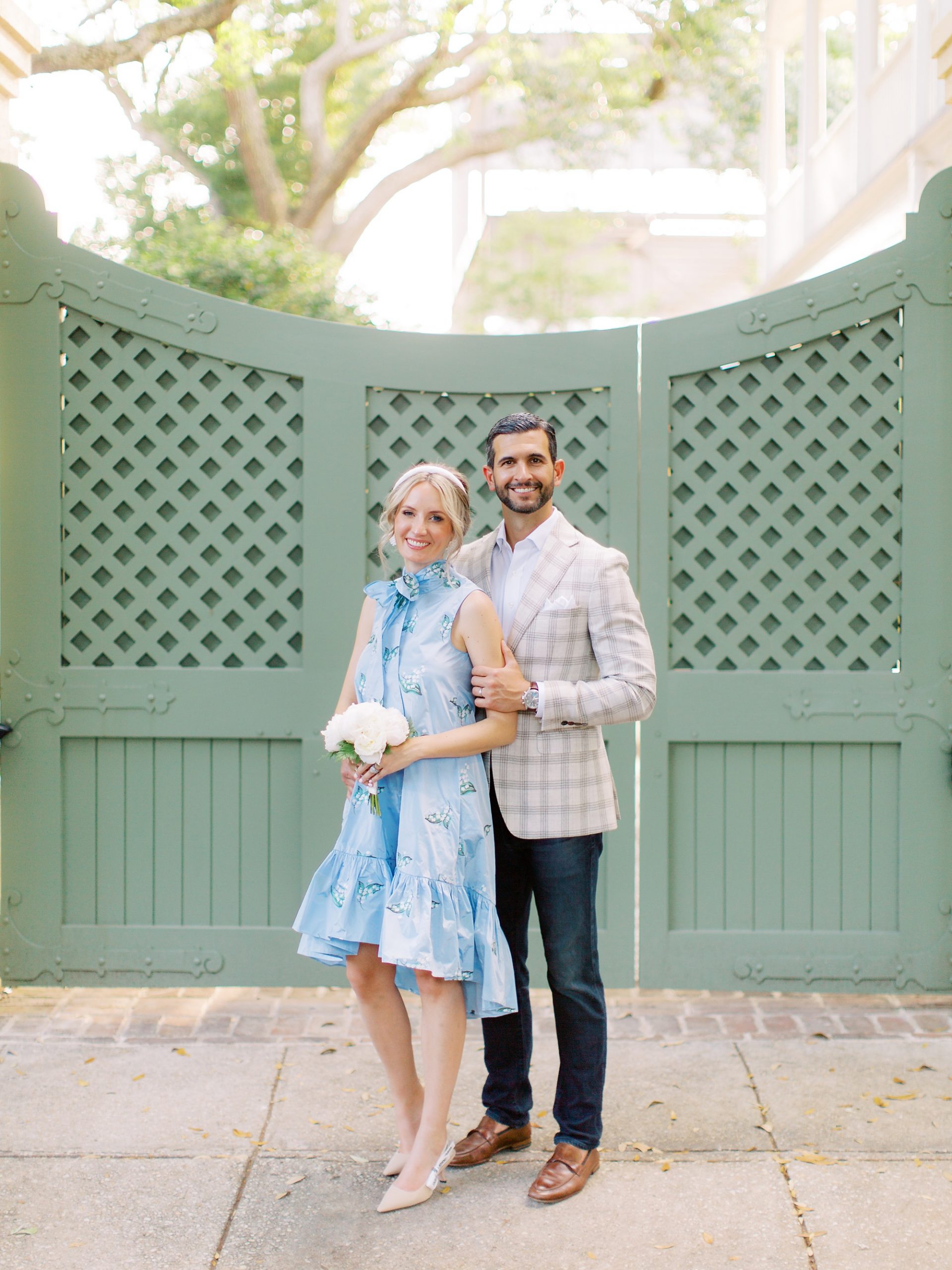 husband and wife pose in front of green gate