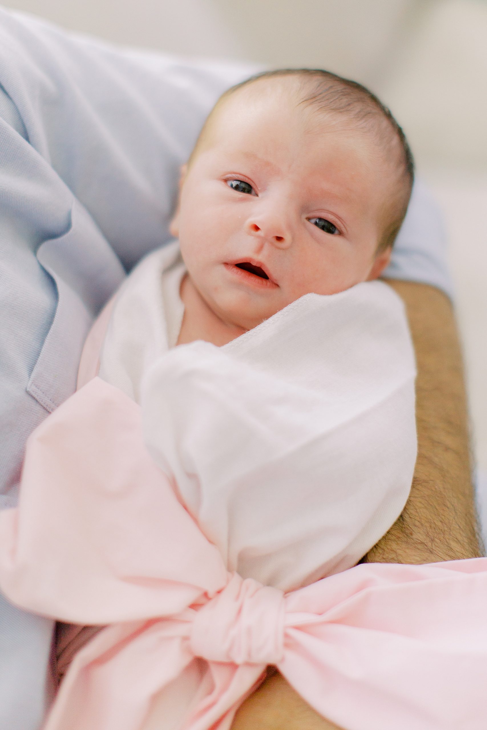baby in white wrap and pink bow looks at camera during Charlotte NC newborn photos