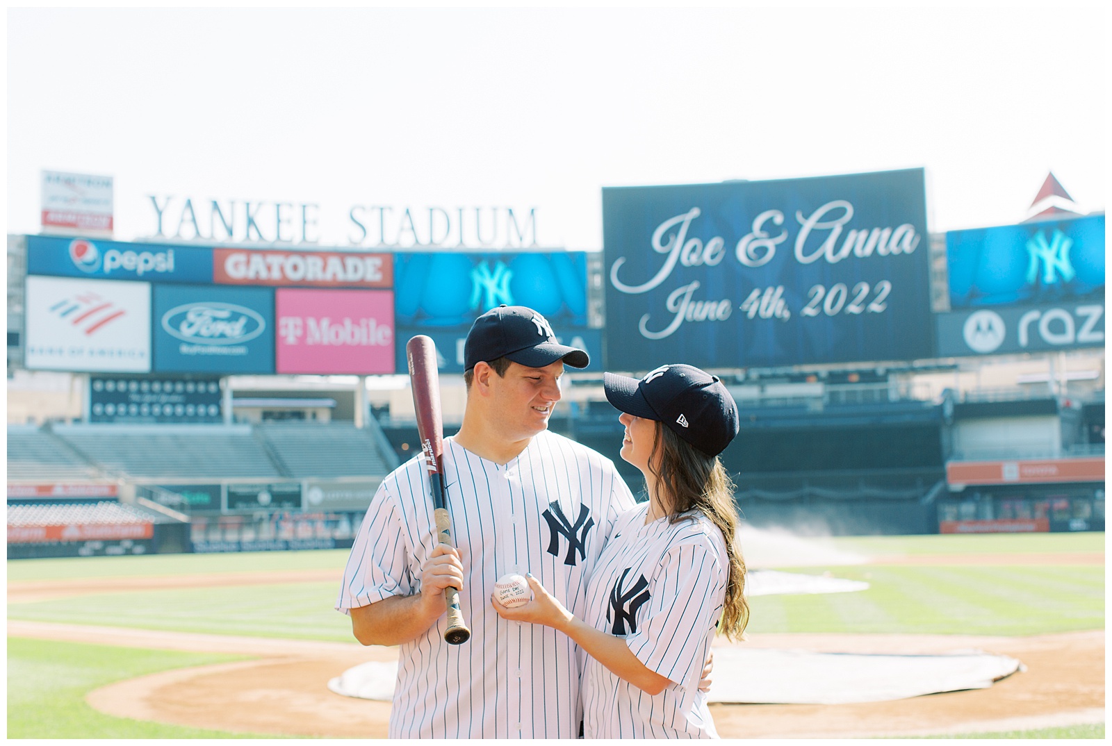 couple holds baseball bat and baseball in Yankee Stadium 