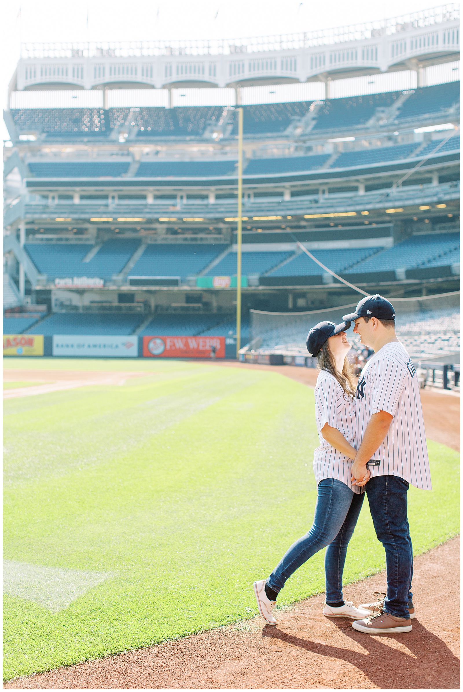 bride and groom hold hands standing inside baseball field during Yankee Stadium Engagement Session