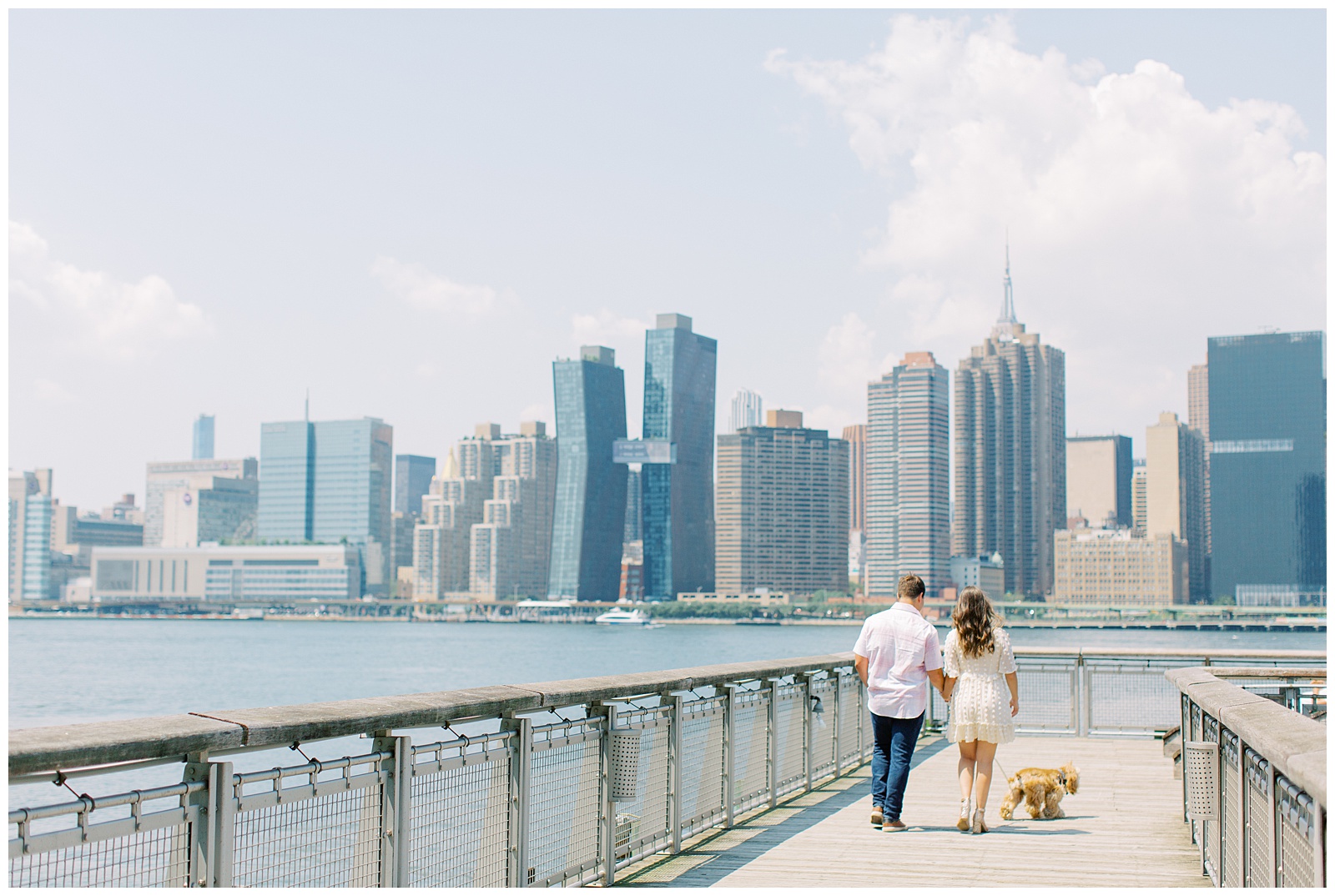 engaged couple walks down pier with dog in New York City during engagement photos 