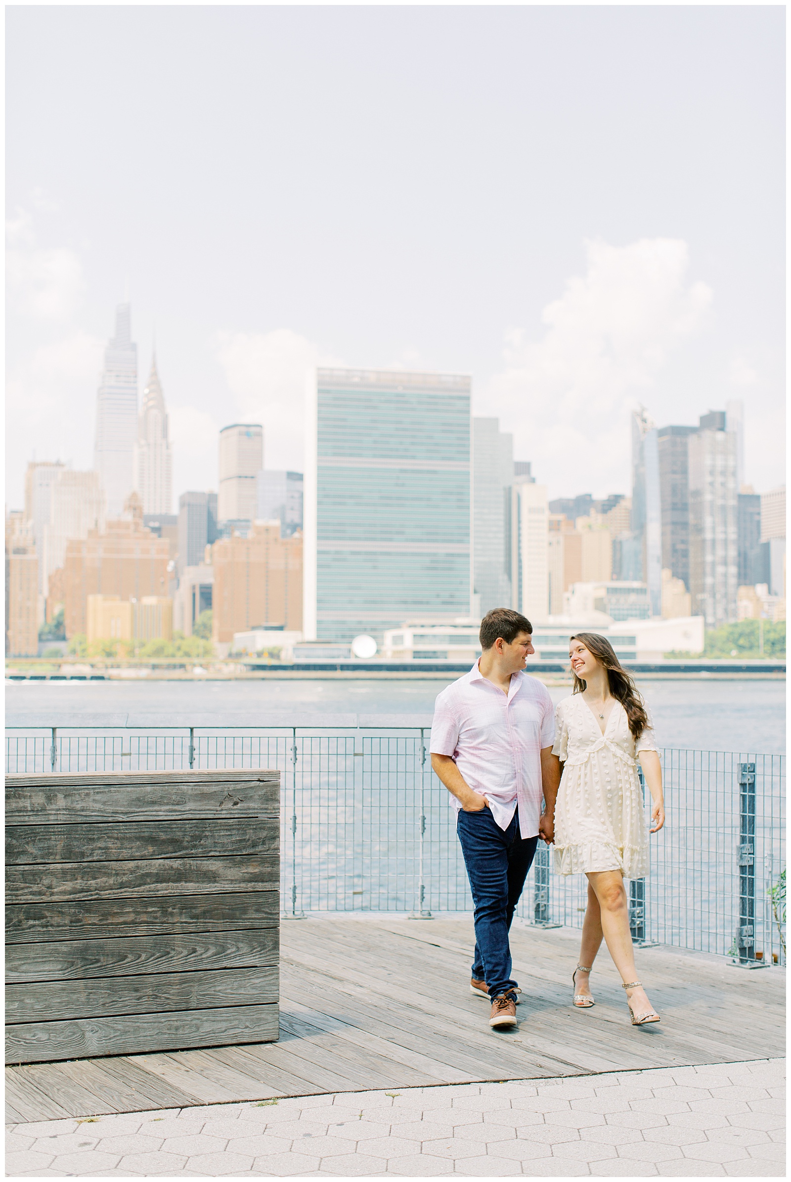 couple walks on pier with Manhattan behind them during NYC engagement session