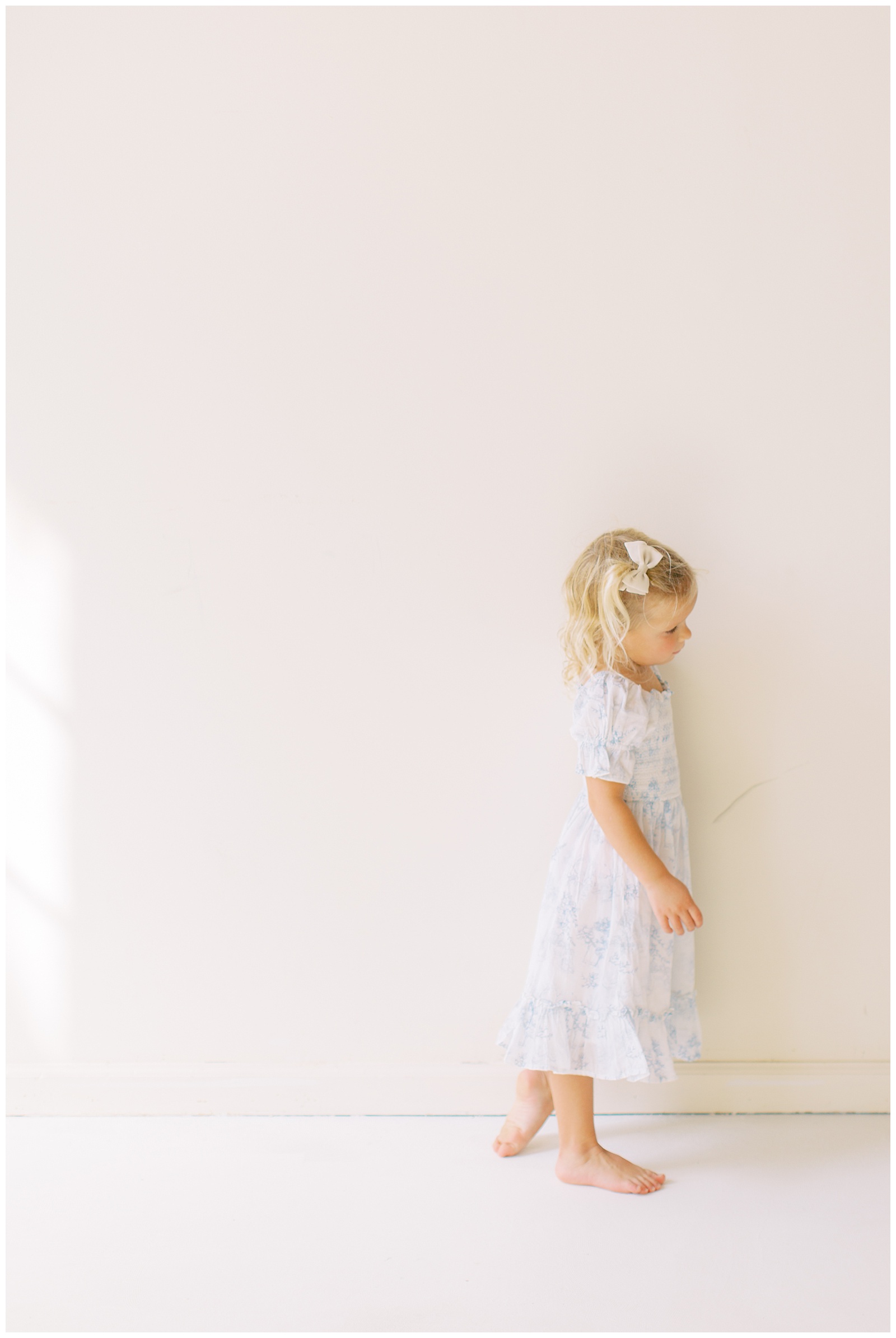 toddler leans against white wall during branding session for mom