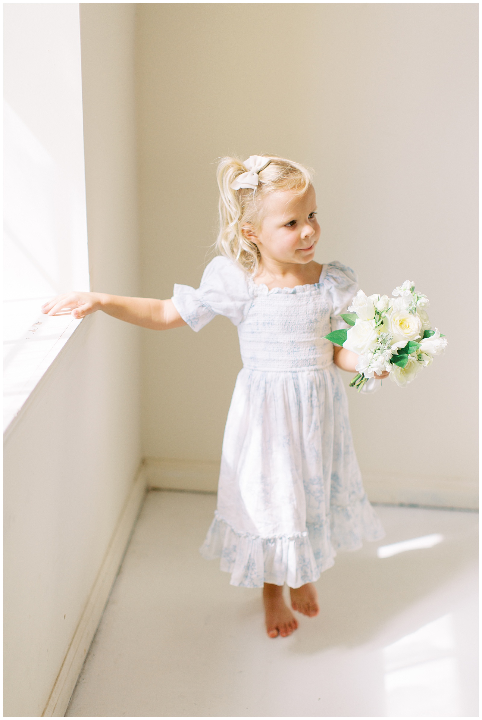 toddler poses by window in light blue and white dress