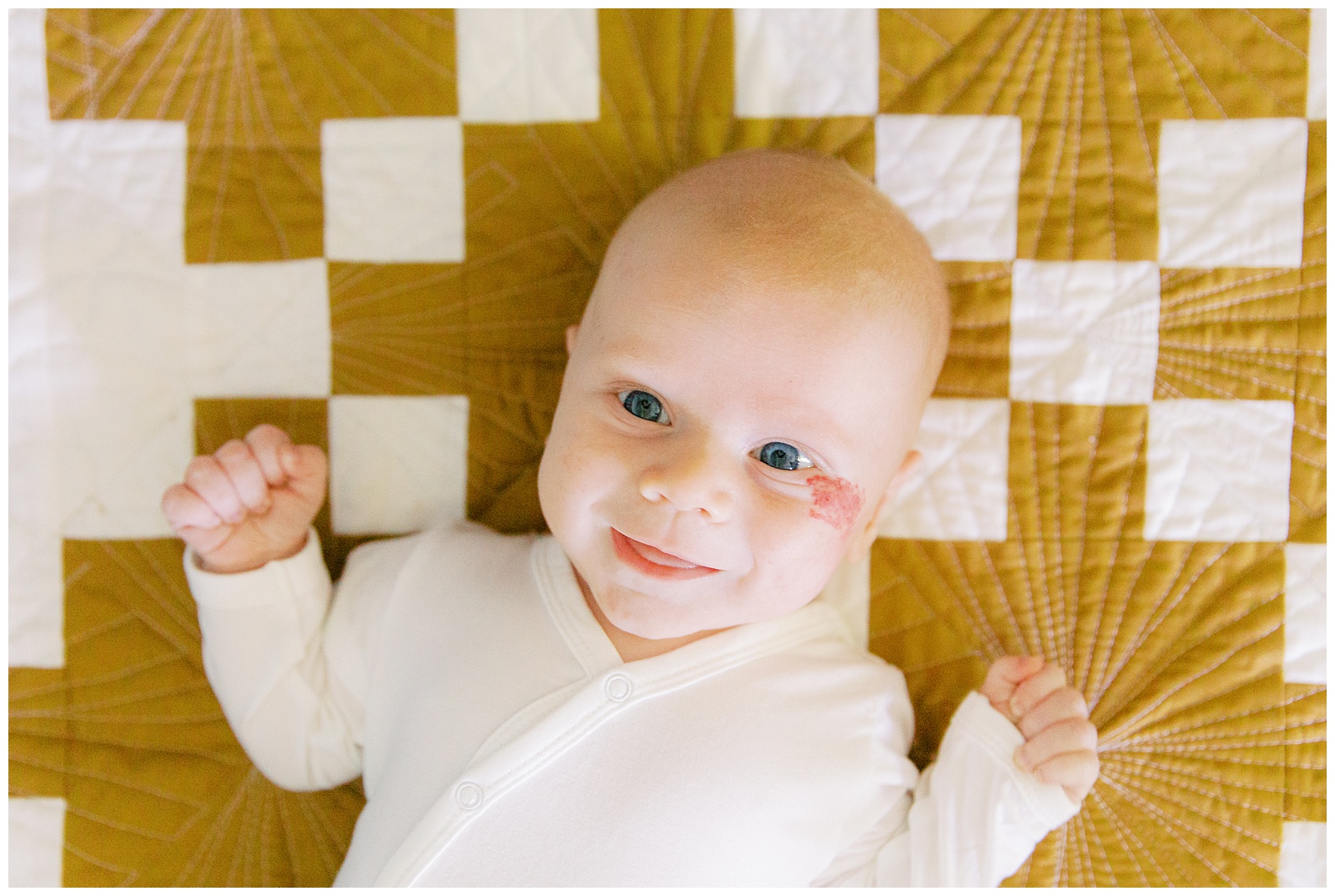 baby smiles laying on gold and white blanket during newborn photos