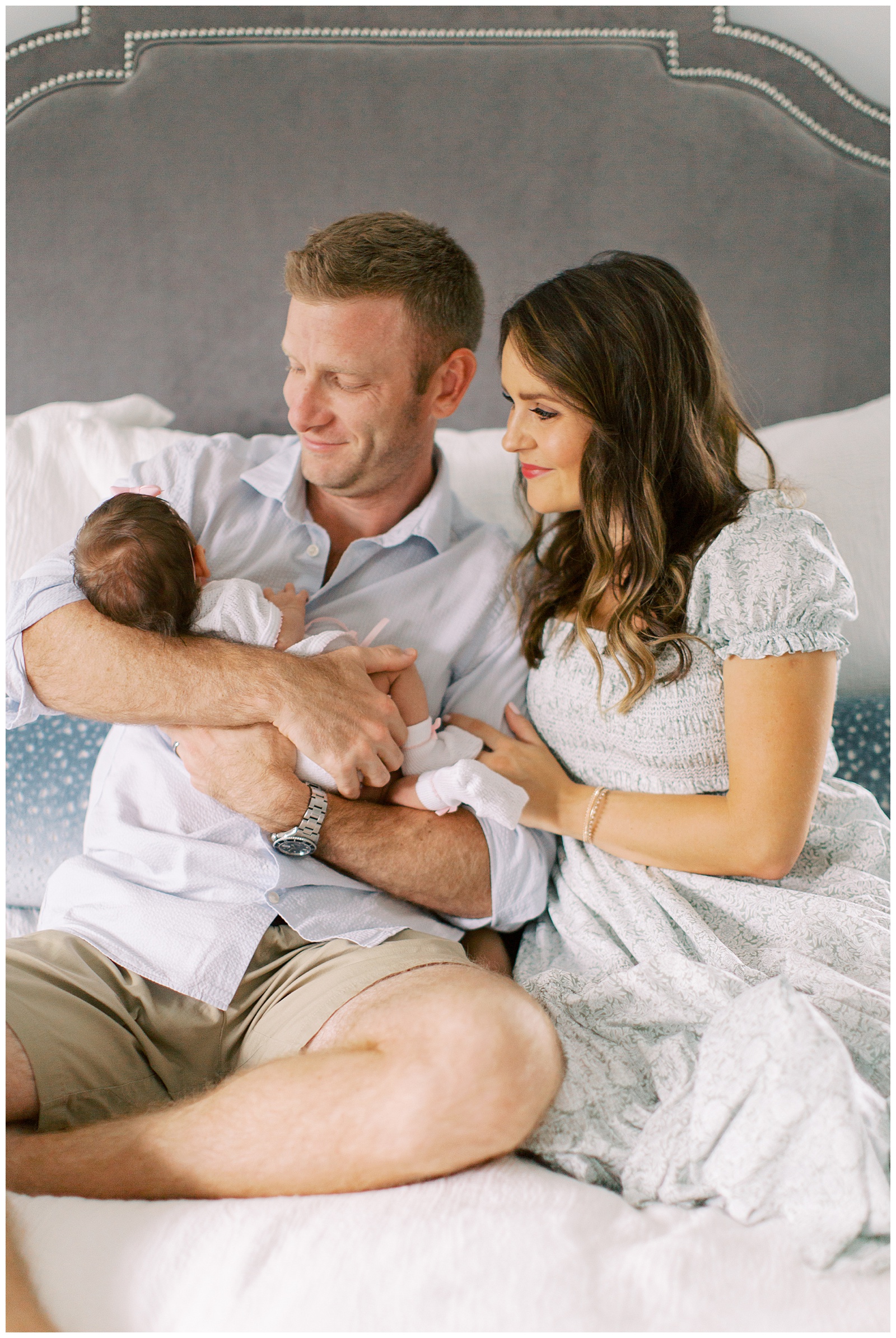 parents look at daughter while sitting on bed during Lifestyle Newborn Session in Charlotte