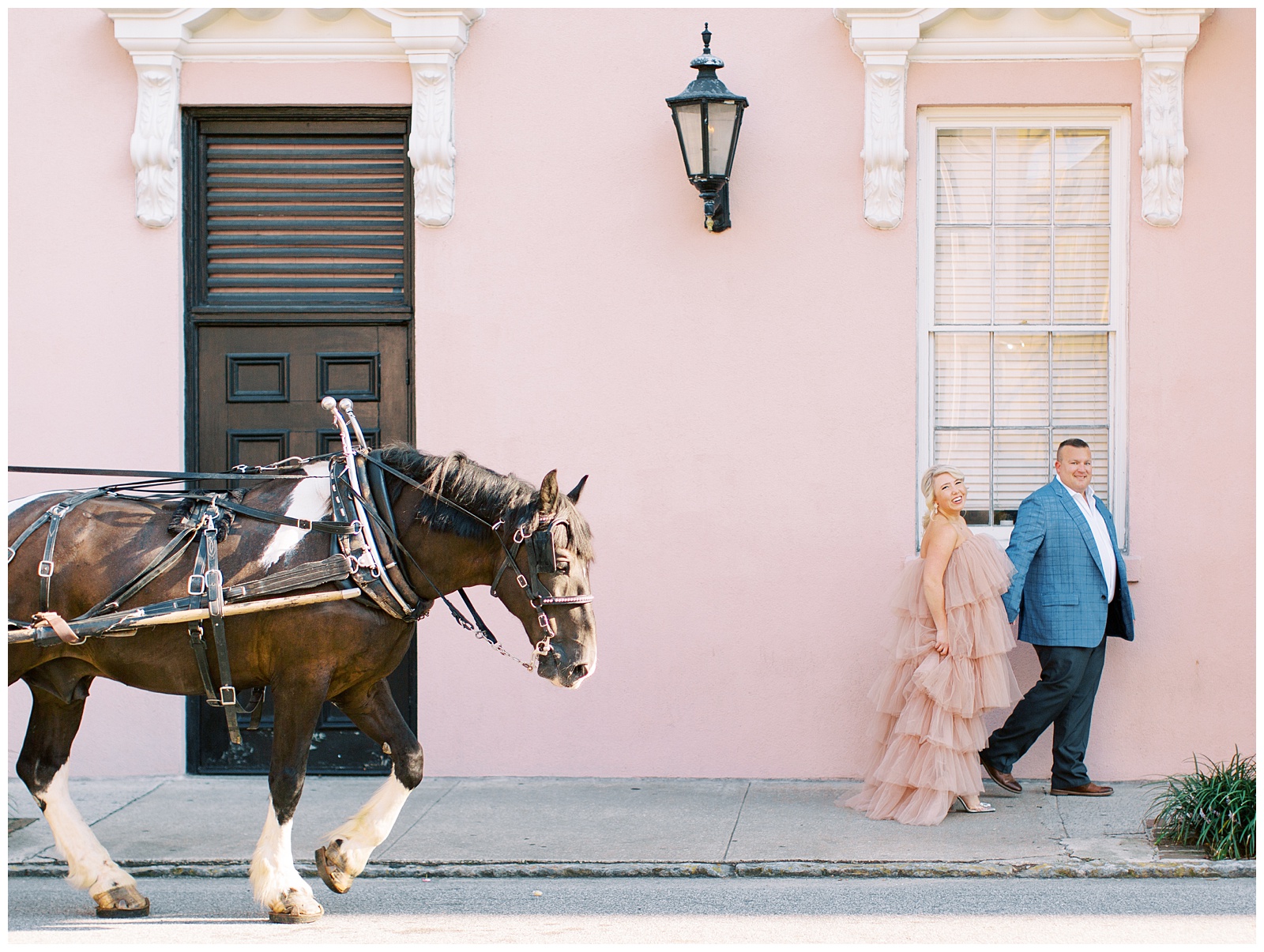 bride and groom walk by pink house with horse during Downtown Charleston engagement session