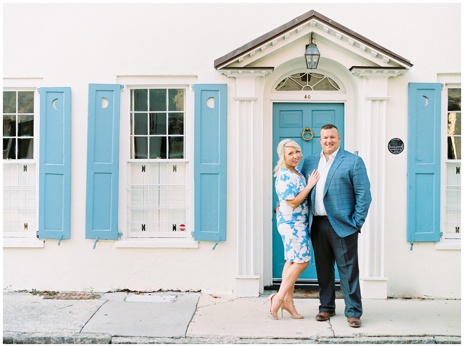 bride and groom pose by blue and white house in Charleston in blue and white outfits