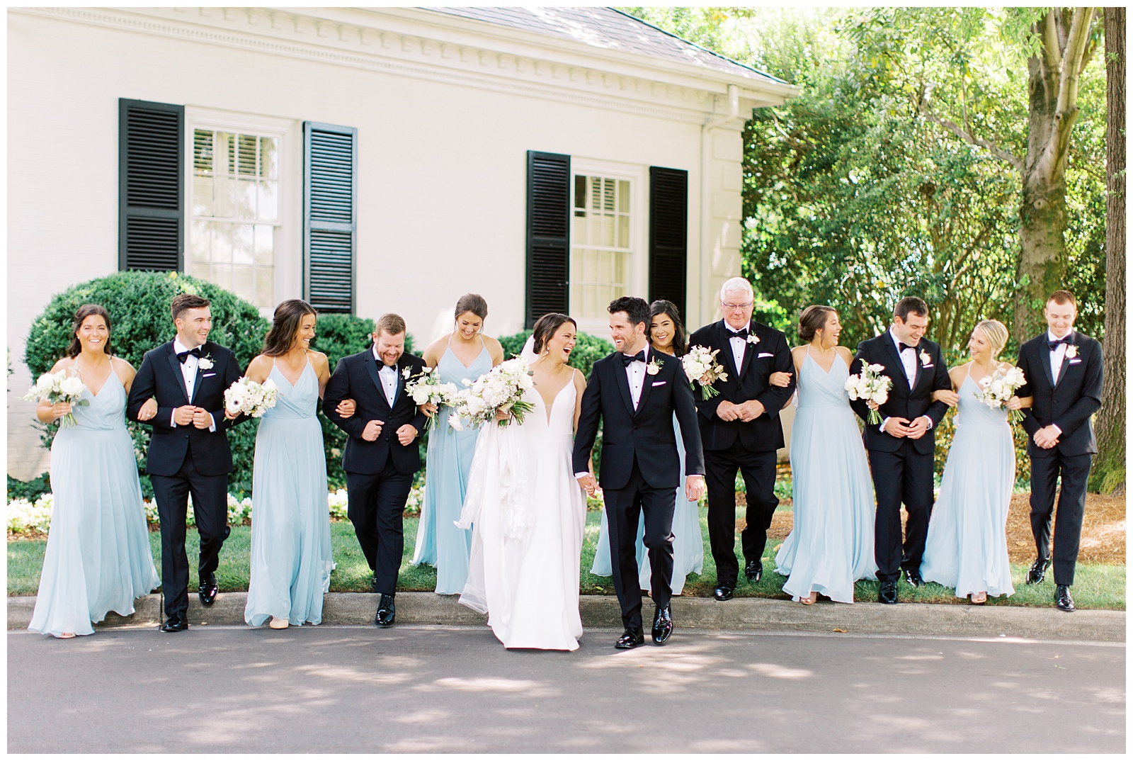 newlyweds walk with wedding party in blue gowns and black tuxes 