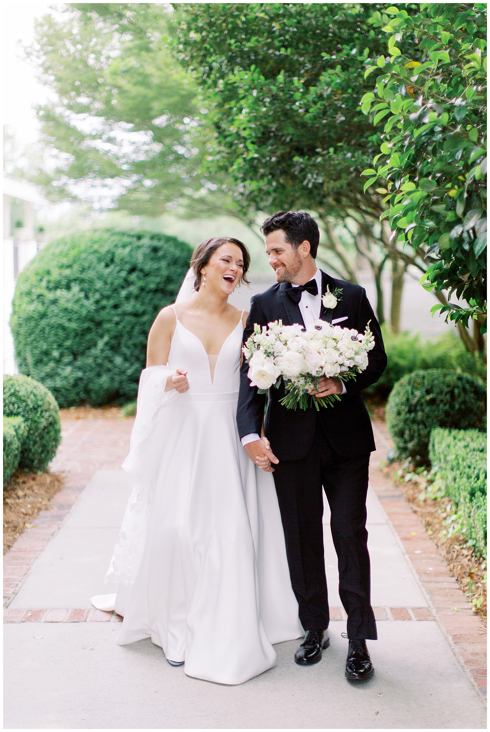 newlyweds hold hands laughing during portraits at Quail Hollow Country Club