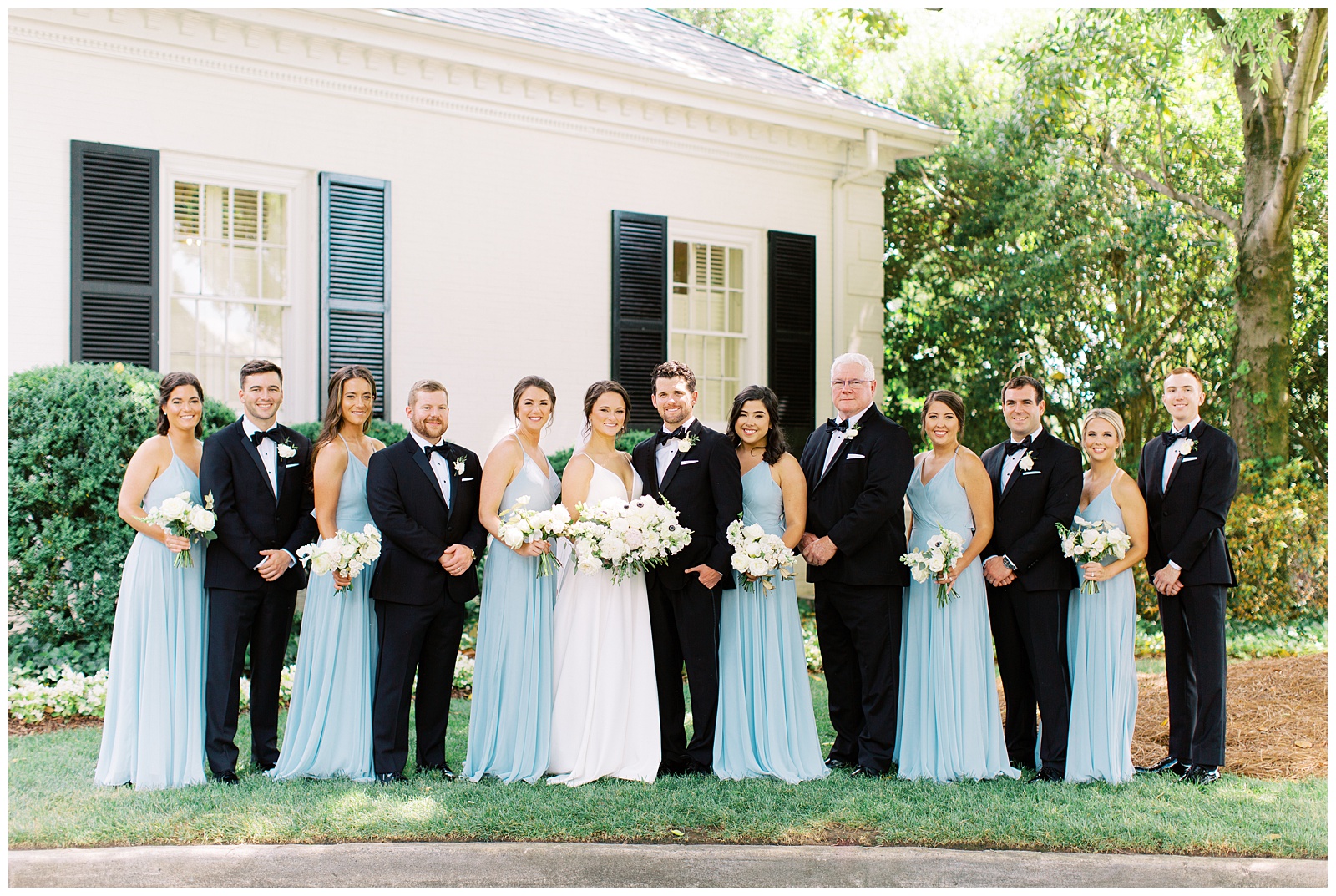 bride and groom pose with bridal party in black tuxes and blue dresses