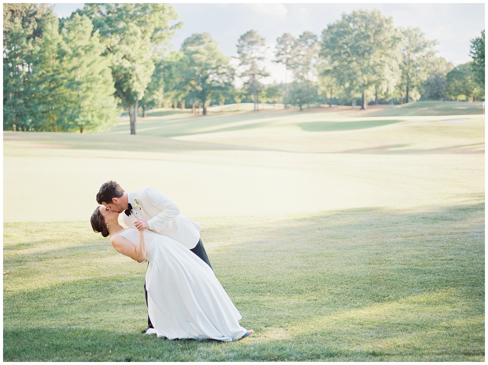 groom dips bride kissing her during Quail Hollow Country Club wedding portraits 