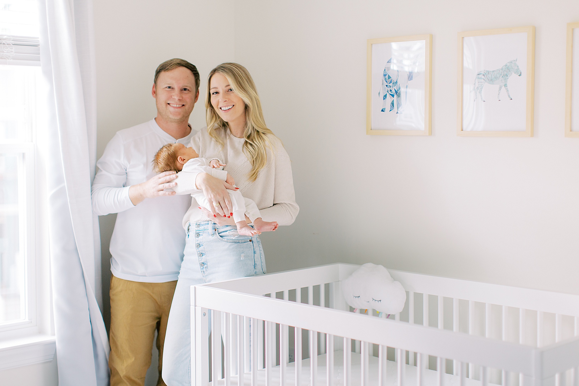 parents pose by crib with baby during newborn photos