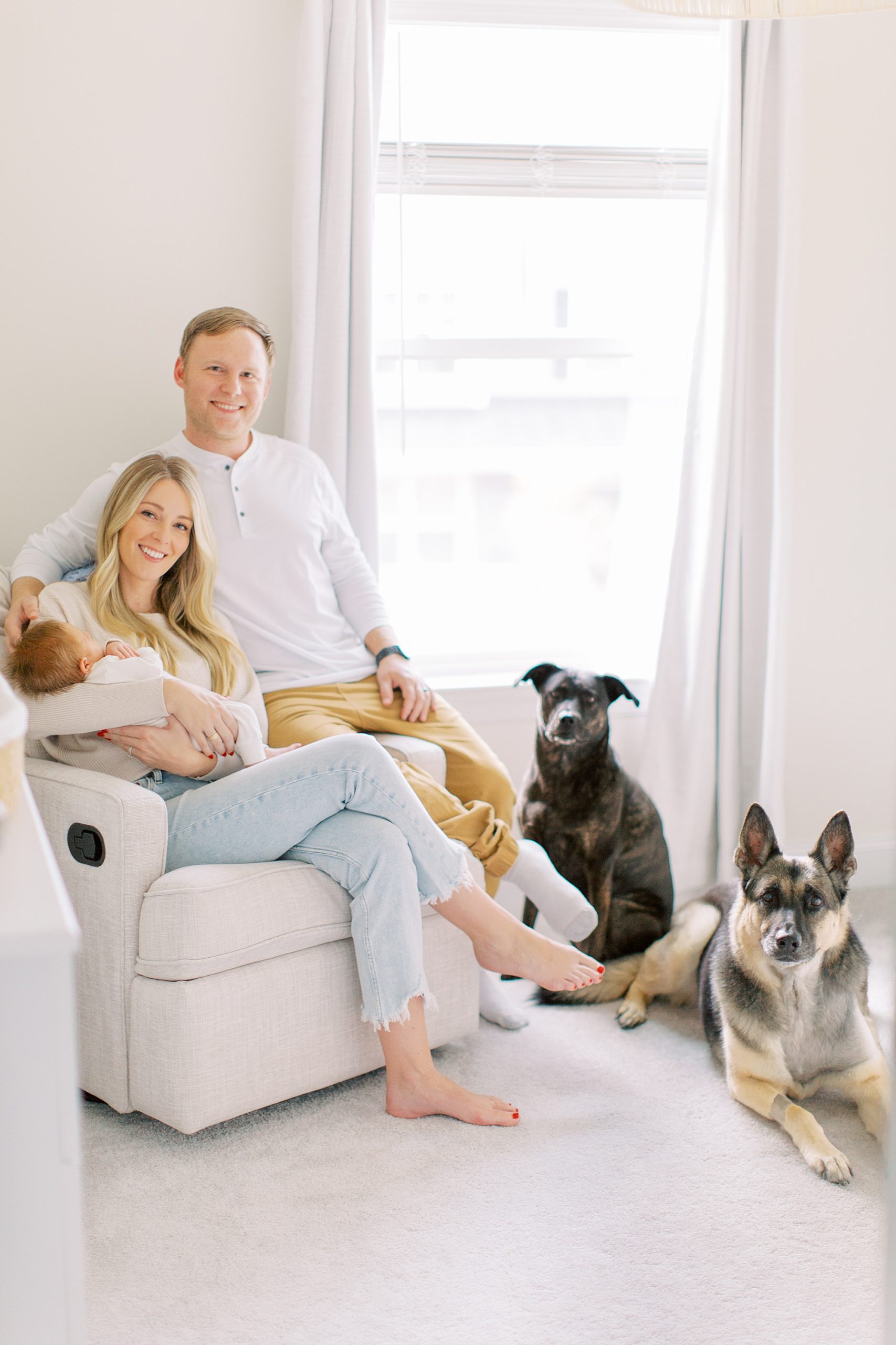 new parents sit in rocker with baby boy and two dogs