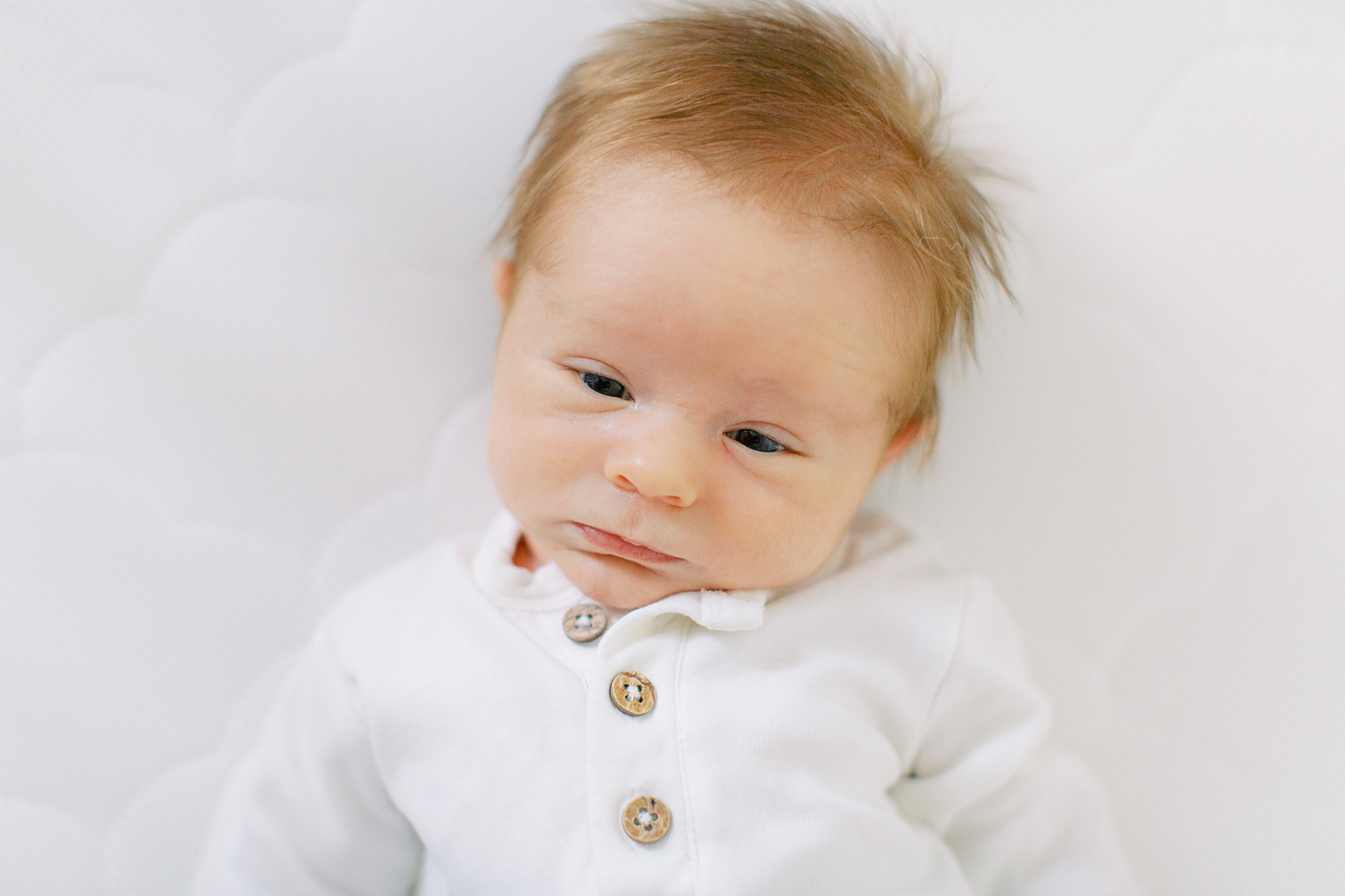 baby lays in white outfit during Charlotte newborn session