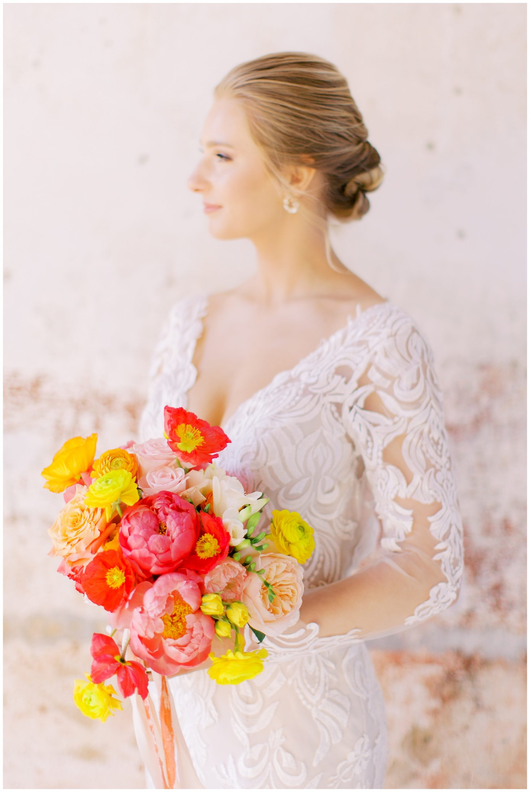 bride holds bouquet with pink and yellow flowers in lace wedding gown for citrus inspired wedding