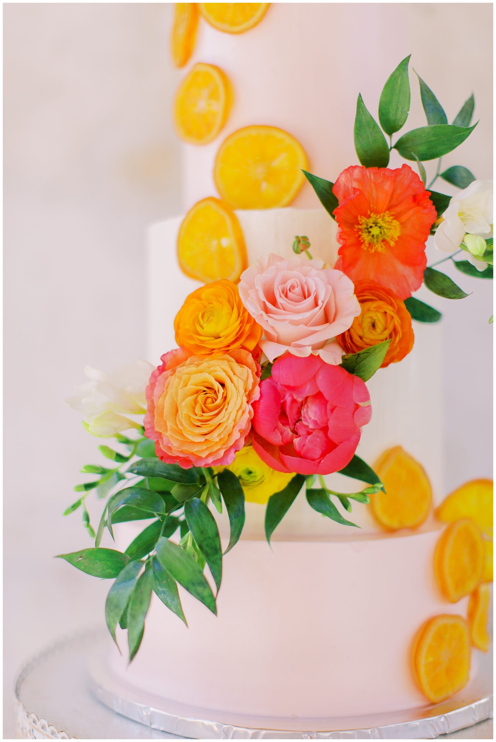 bright flowers wrapped down cake with citrus slices for citrus inspired wedding