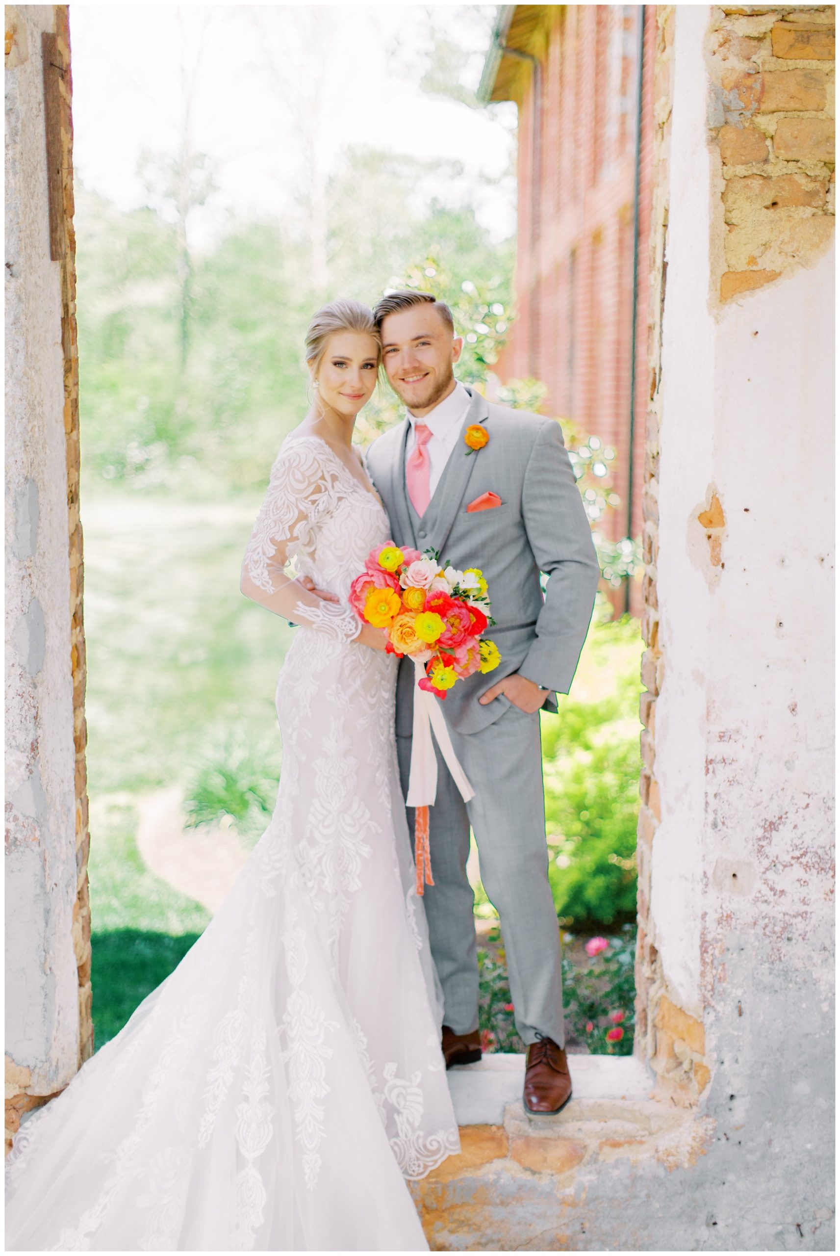 bride and groom stand in window of Providence Cotton Mill with bright bouquet 