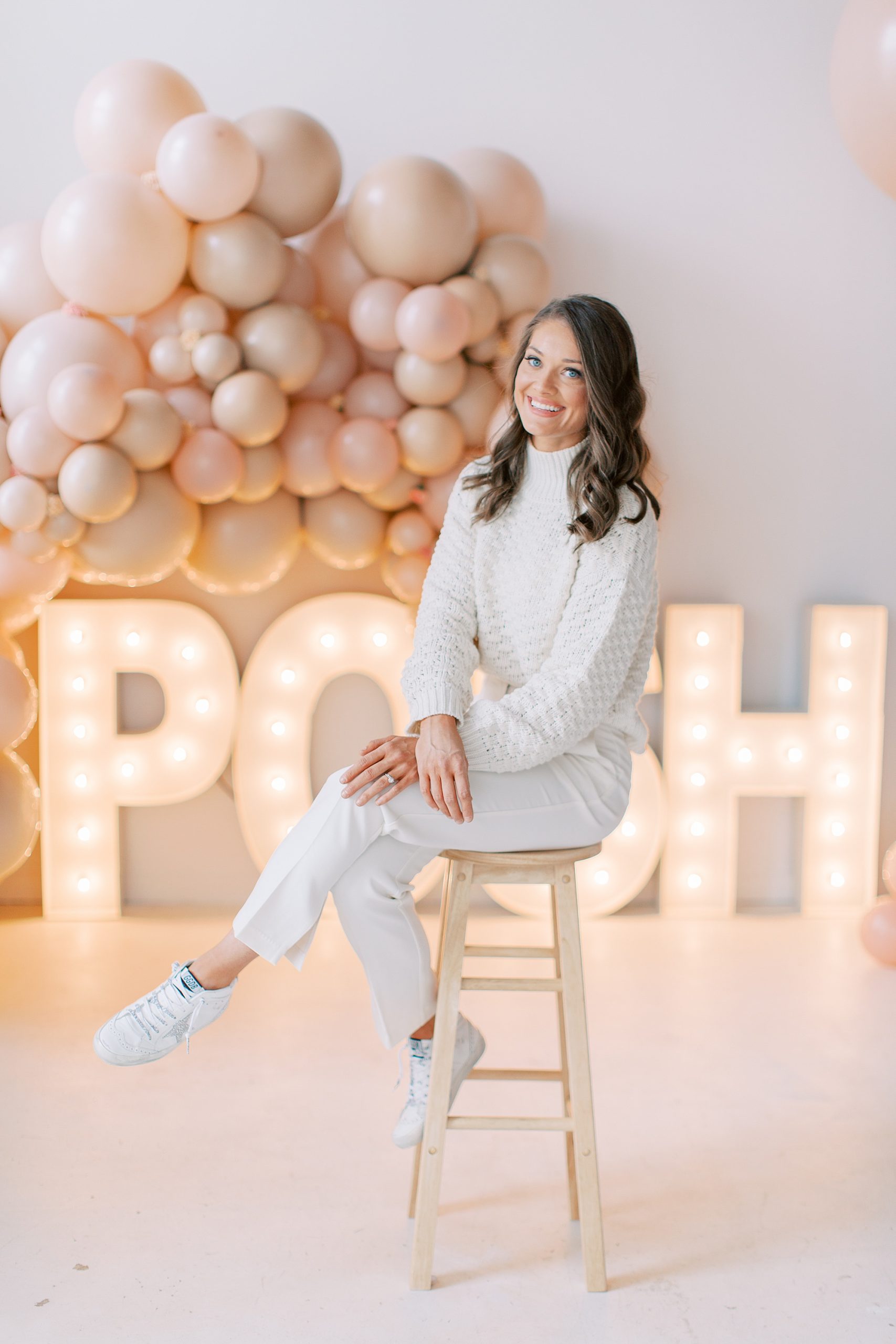woman sits on stool by POSH sign and balloon arch