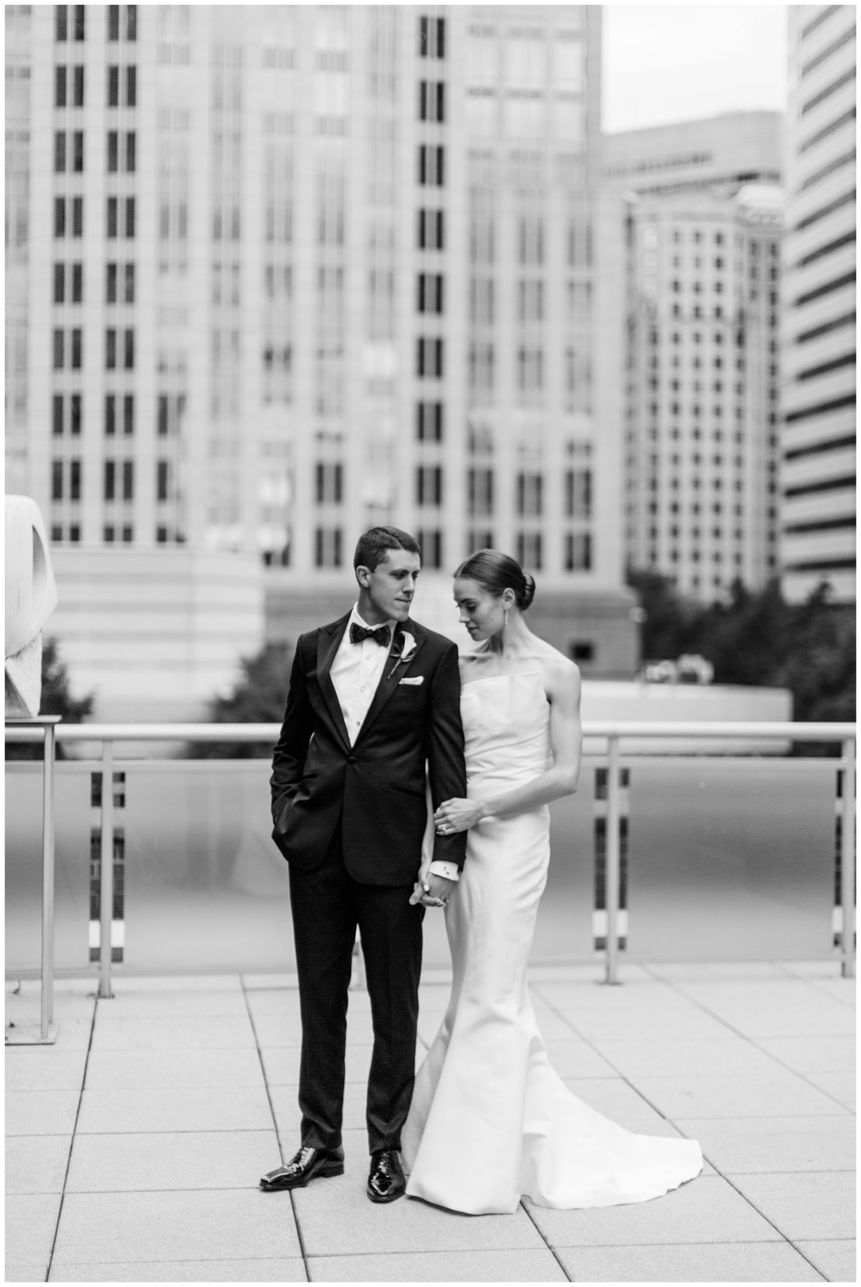 bride and groom hold hands on balcony at the Foundation for the Carolinas with Charlotte skyline behind them
