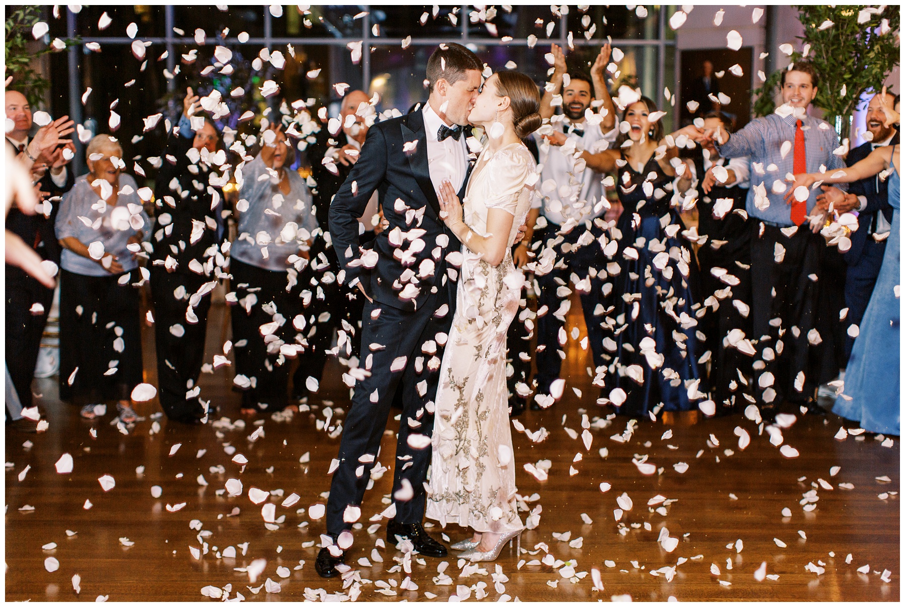 couple kisses on dance floor while petals fall during Charlotte wedding reception
