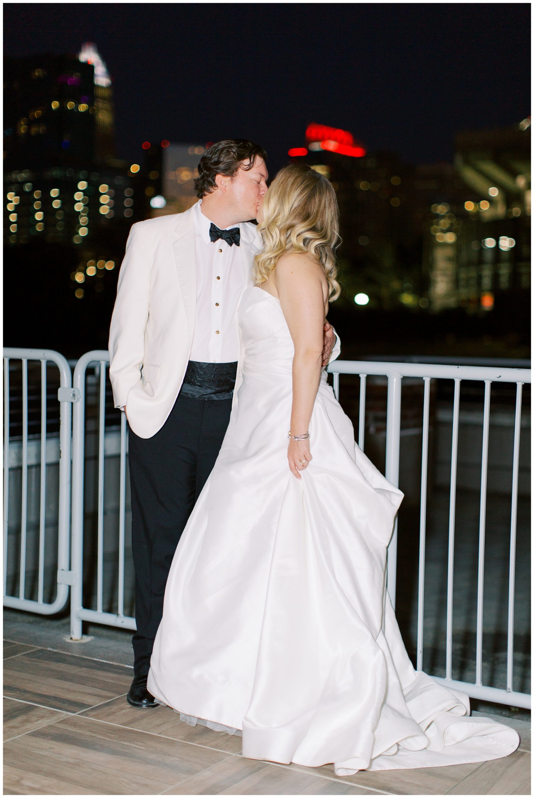 newlyweds kiss on balcony at The Terrace at Cedar Hill with Charlotte NC skyline behind them 