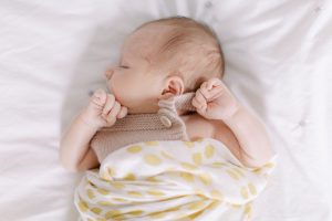 baby lays on bed with hands in fists