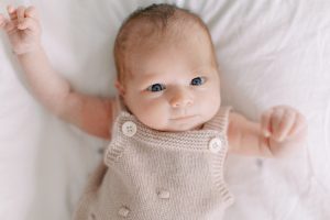 baby lays in tan jumper on bed during newborn photos