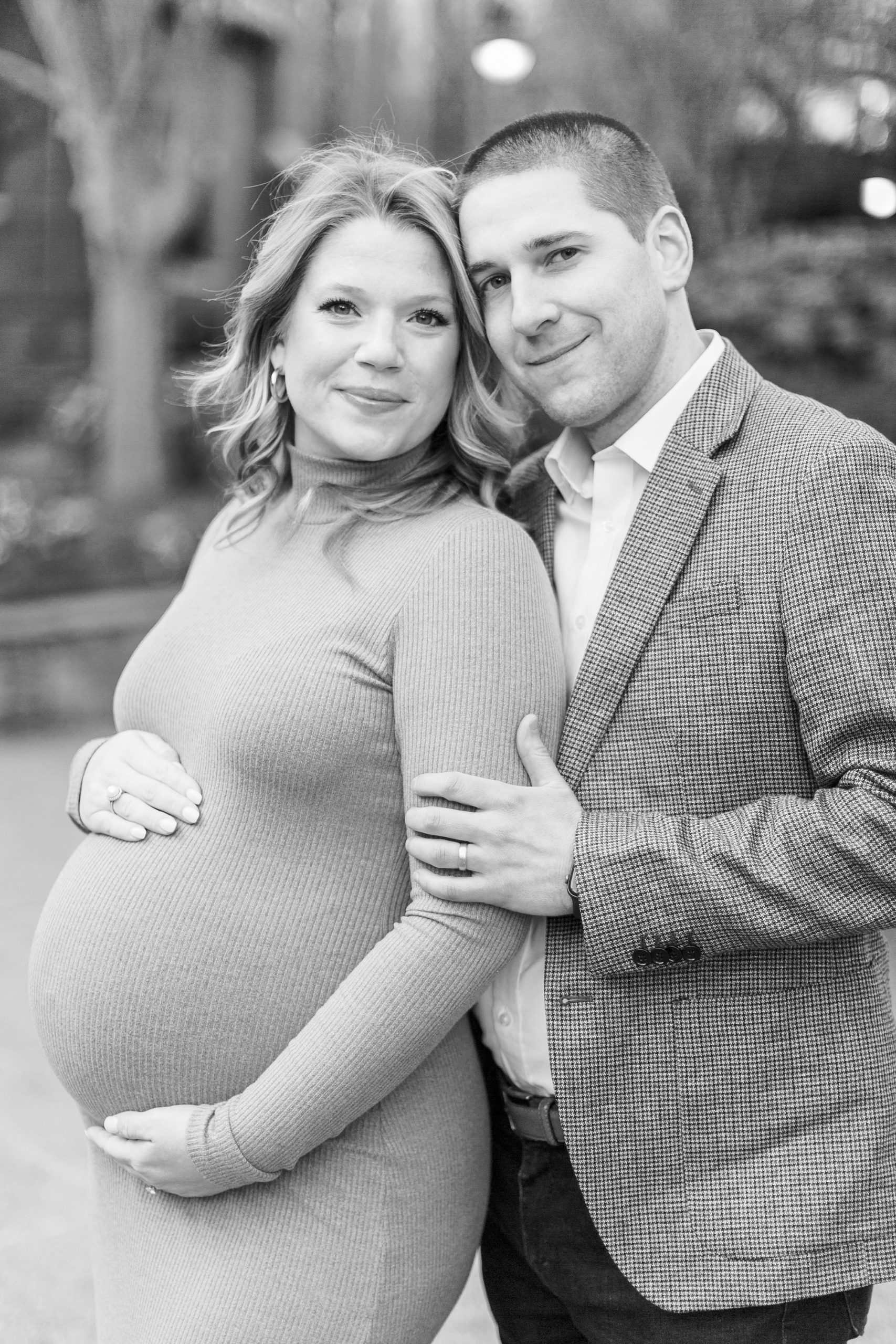 woman leans into husband's arms during Uptown Charlotte maternity session