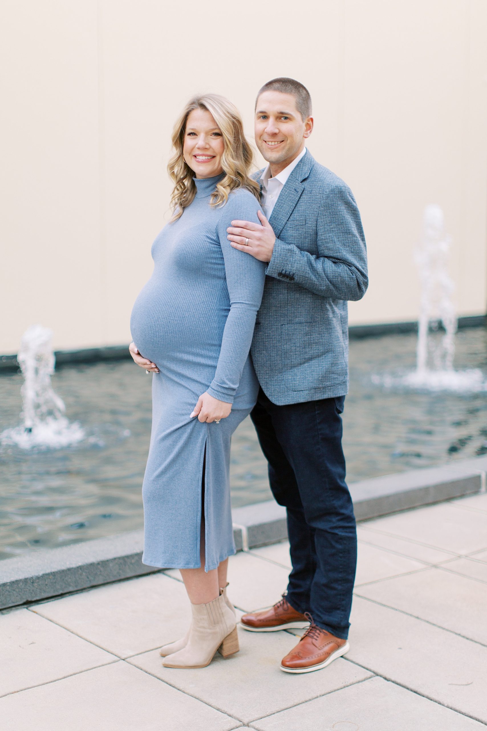 couple poses by fountains during Uptown Charlotte maternity session