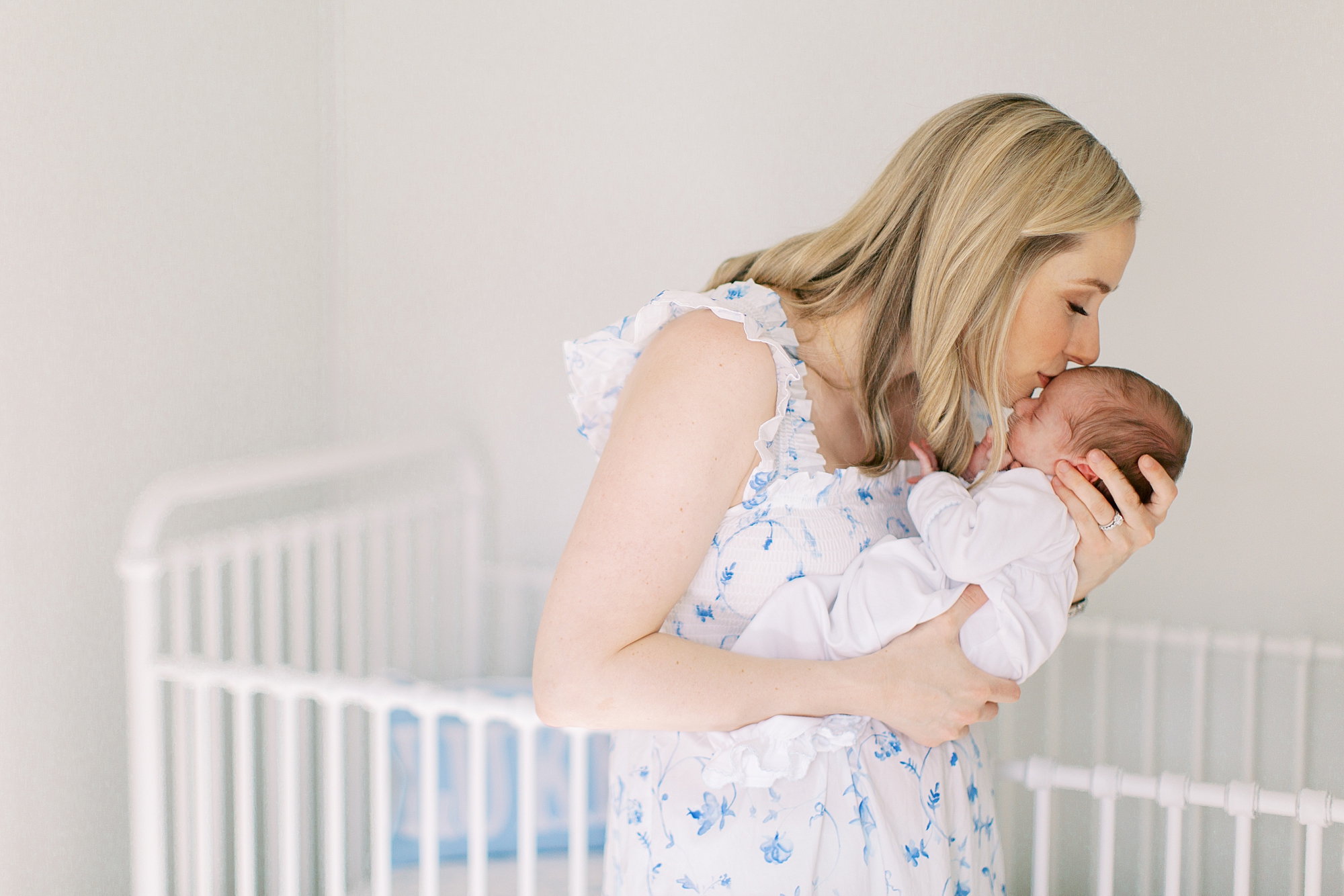 mom kisses baby boy next to crib during lifestyle newborn session in Charlotte NC