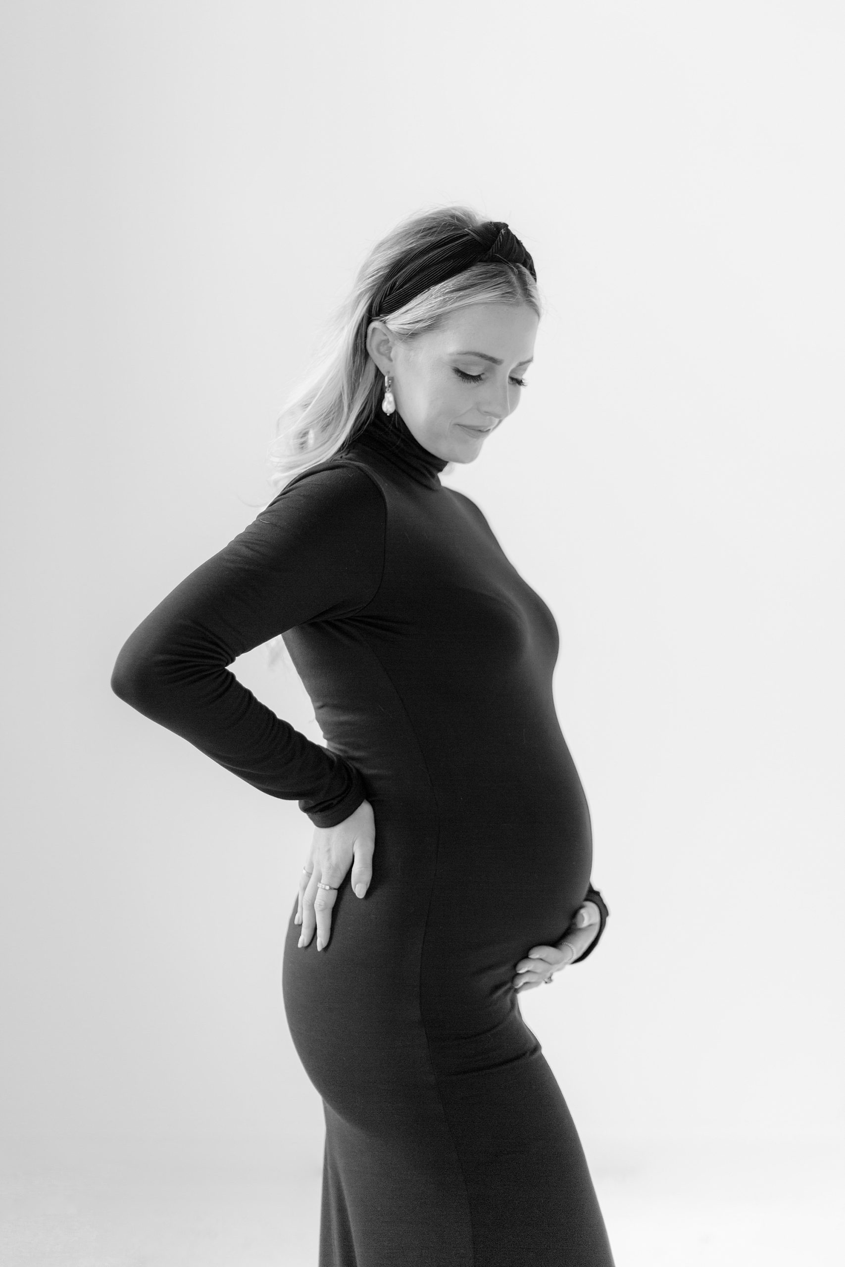 woman stands holding baby bump in chic black dress