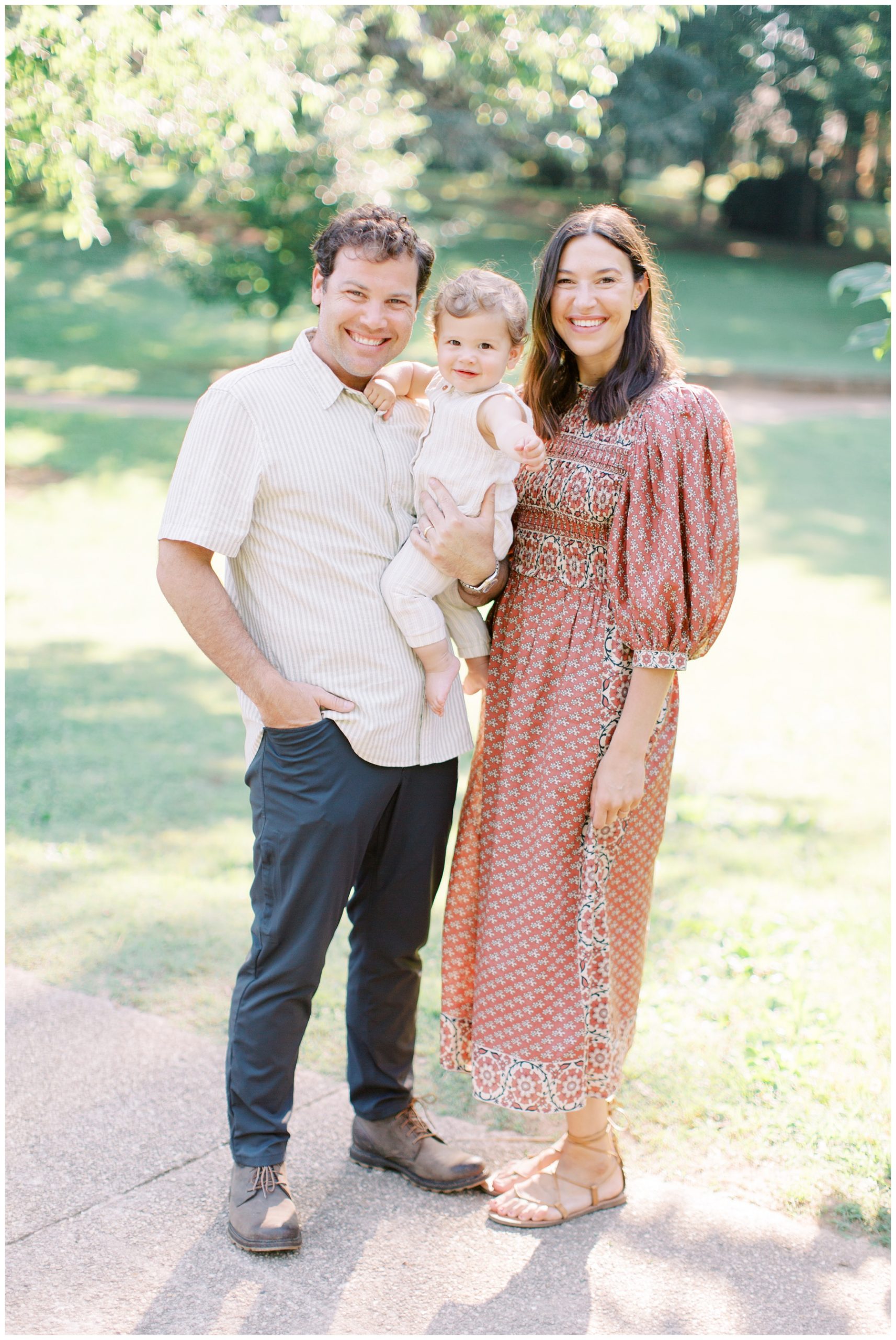 family of three stands together under trees during family session in Charlotte NC