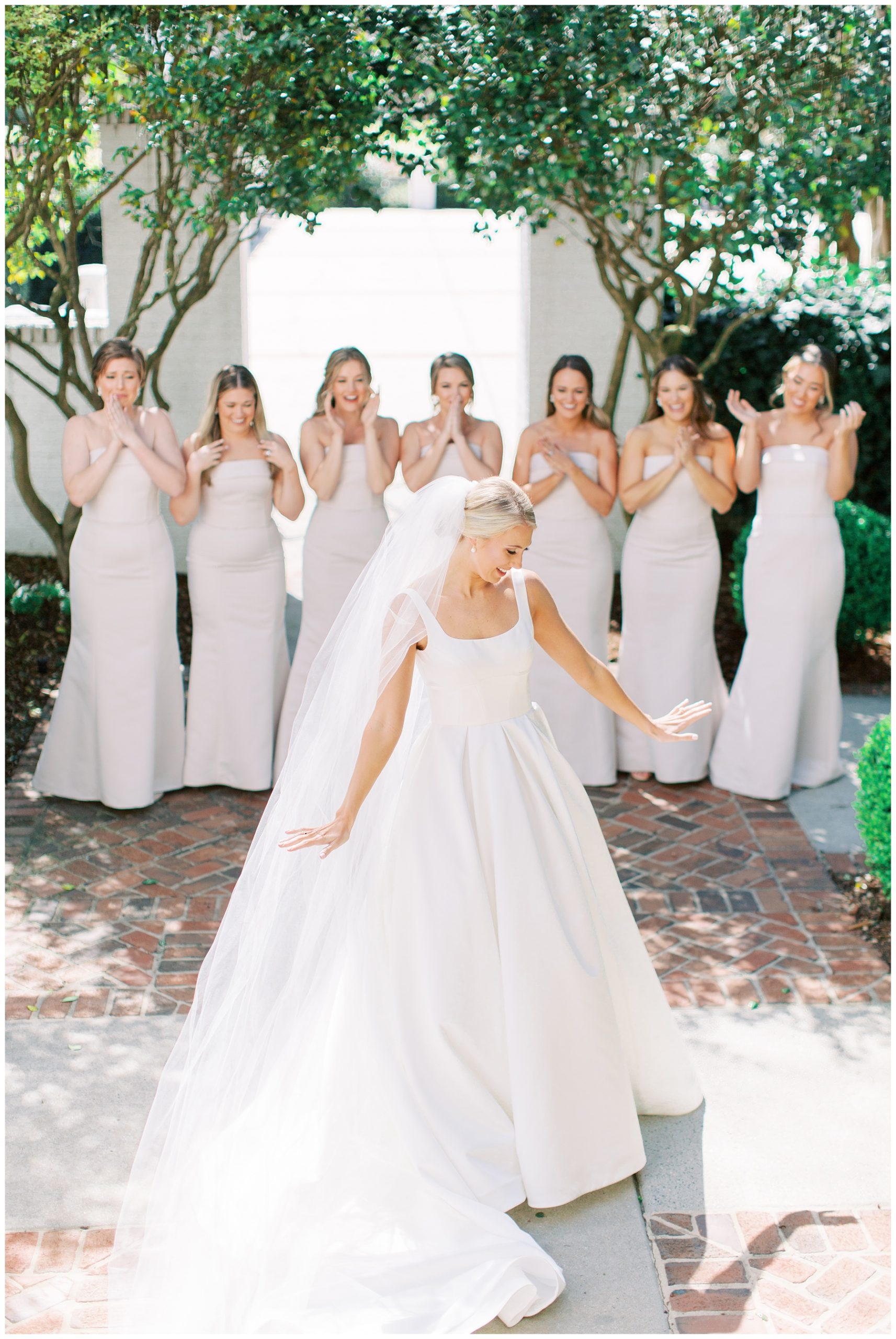 bride shows off wedding gown and veil to bridesmaids during first look