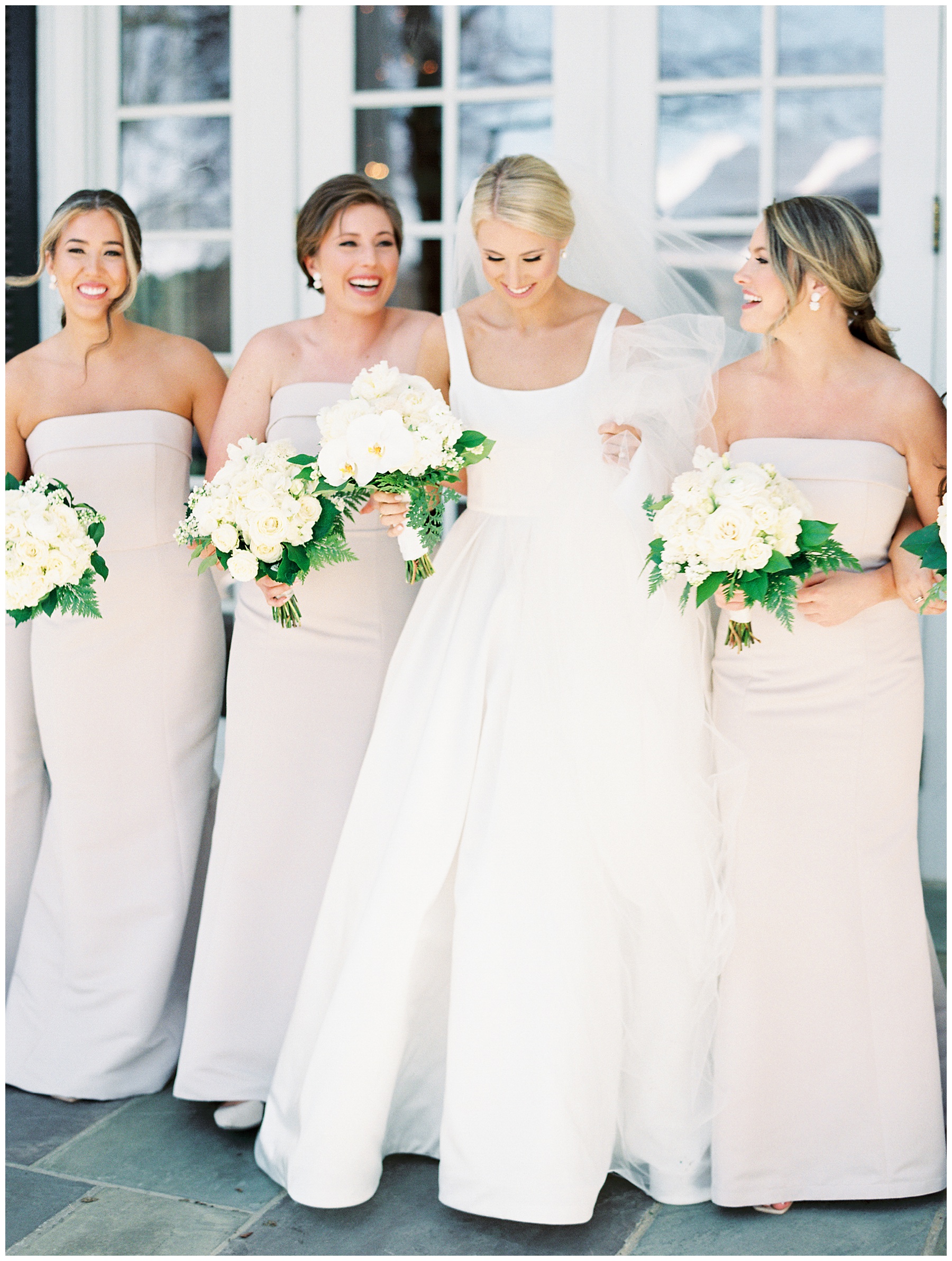 bride laughs walking with bridesmaids in strapless pastel gowns