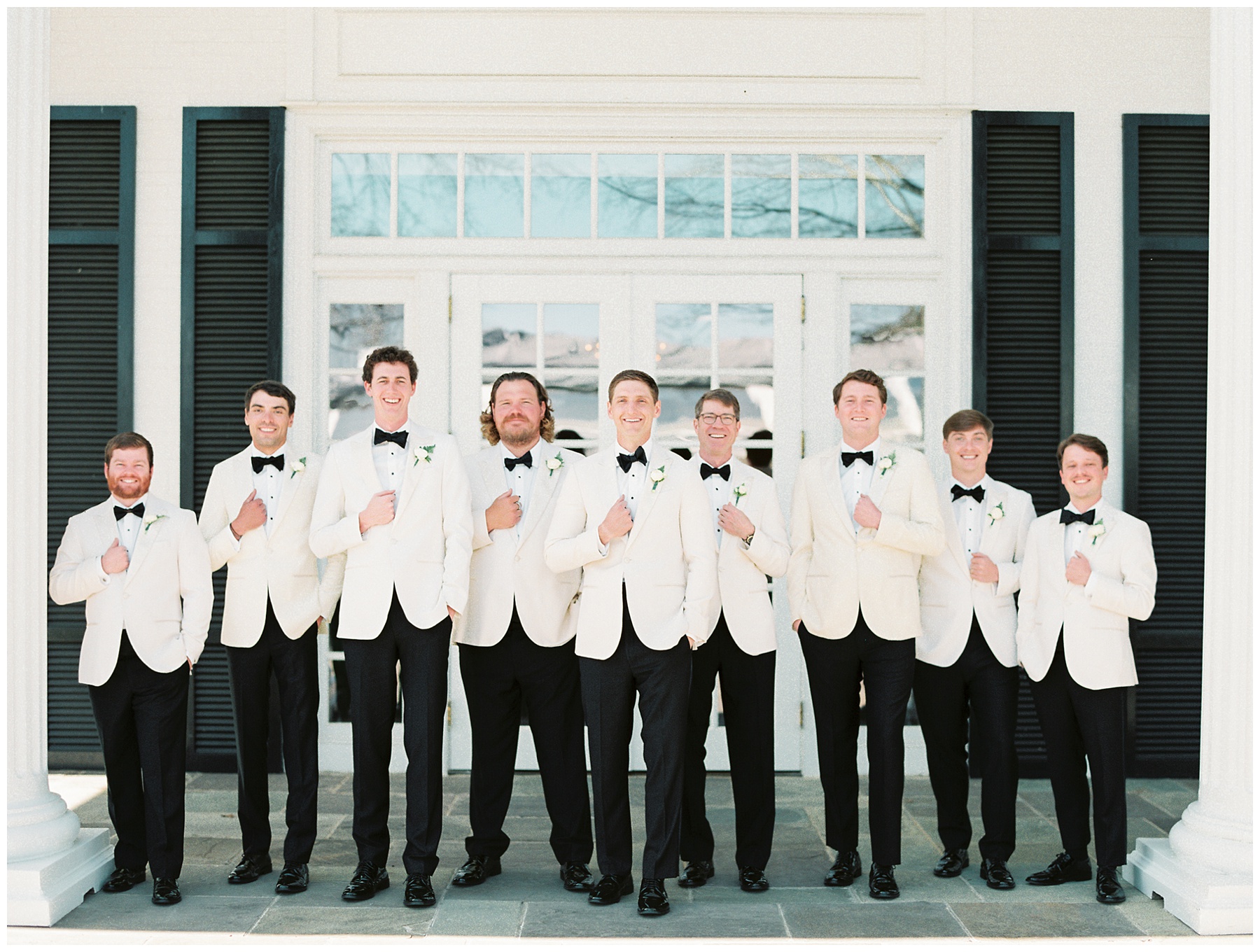 groom stands in white tux jacket with groomsmen on patio at Quail Hollow Club