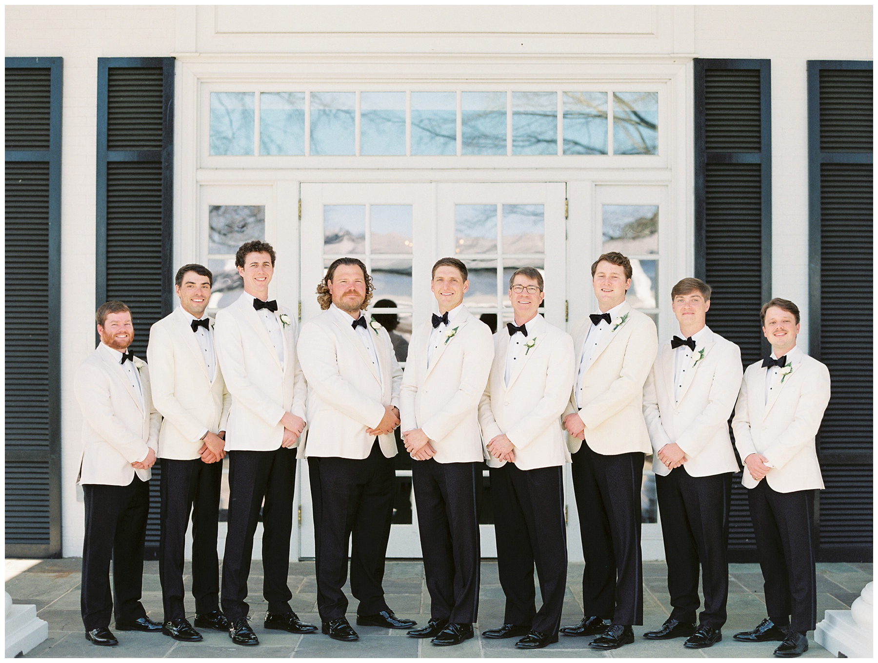 groom stands with groomsmen in white tux jackets outside Quail Hollow Club