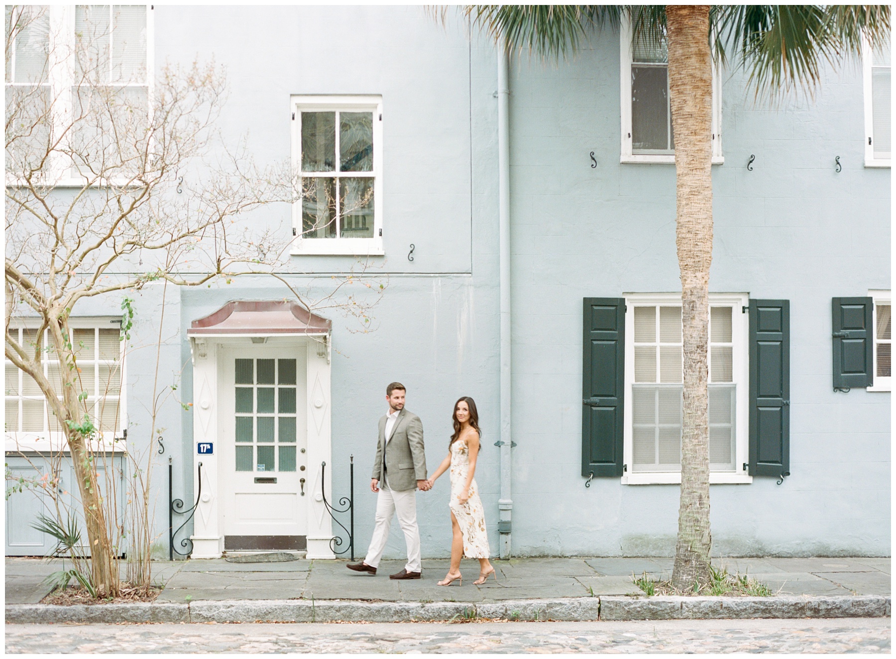 bride in floral dress holds hands with groom walking down Rainbow Row homes in Downtown Charleston