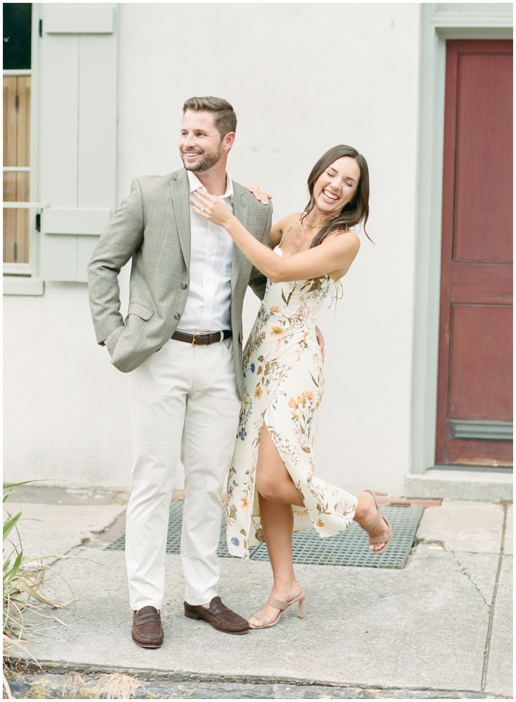 bride and groom laugh during engagement portraits on sidewalk in Downtown Charleston