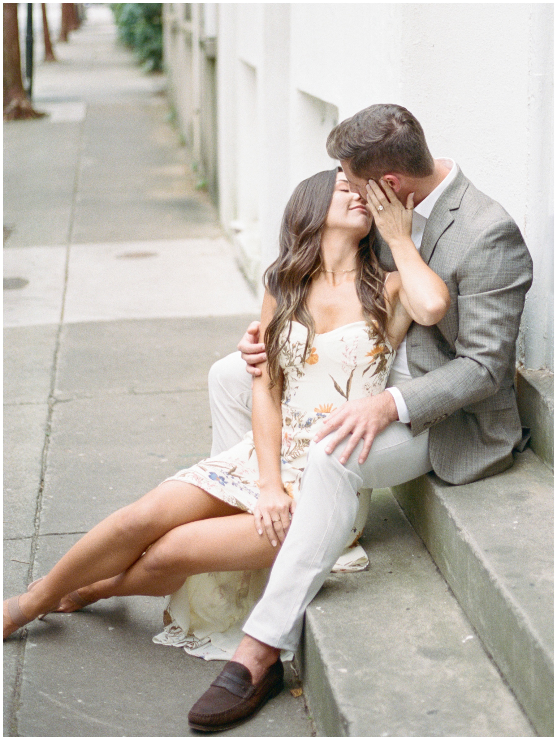 bride sits in between groom's legs on steps leaning up to kiss him 