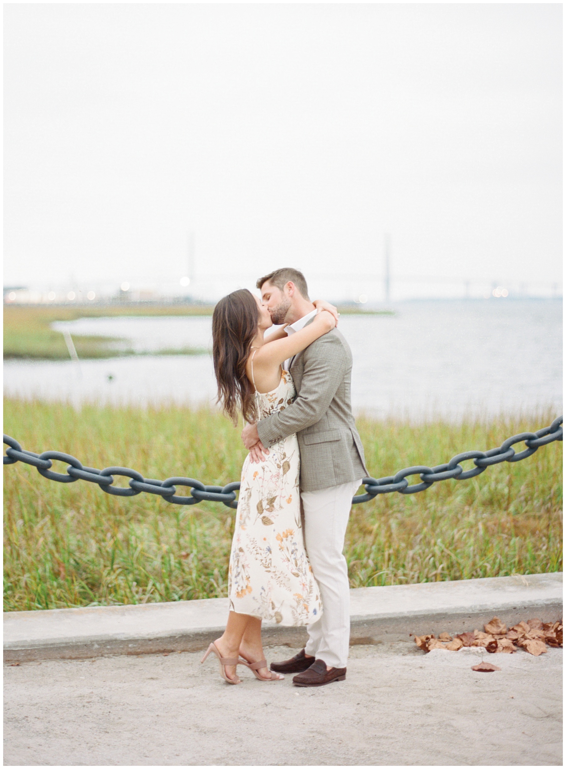 bride hugs groom kissing him in front of chain fence along waterfront in Charleston SC