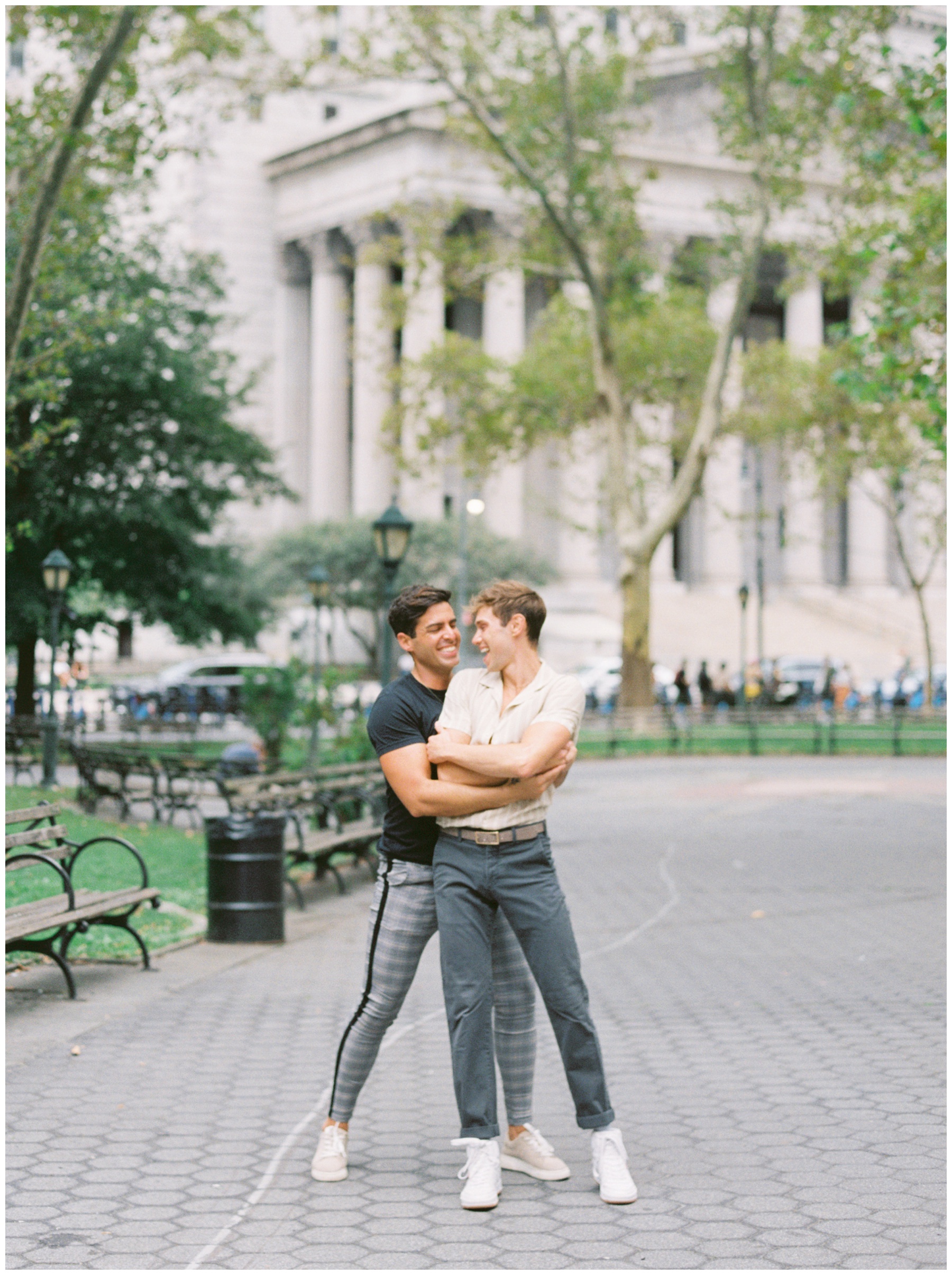 man hugs boyfriend around the waist during New York City engagement session