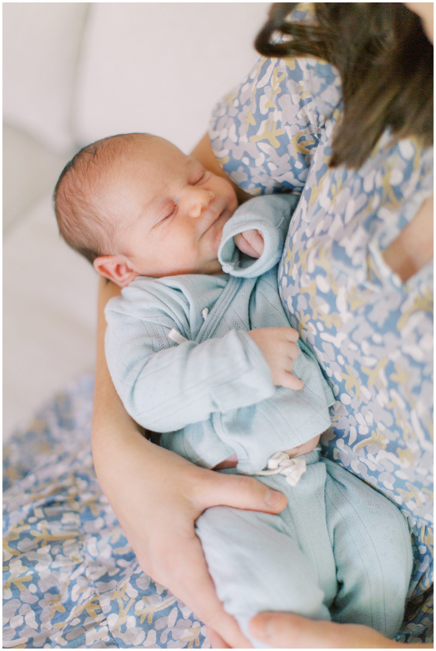 mom in blue, white, and yellow dress holds newborn son against chest on white couch 
