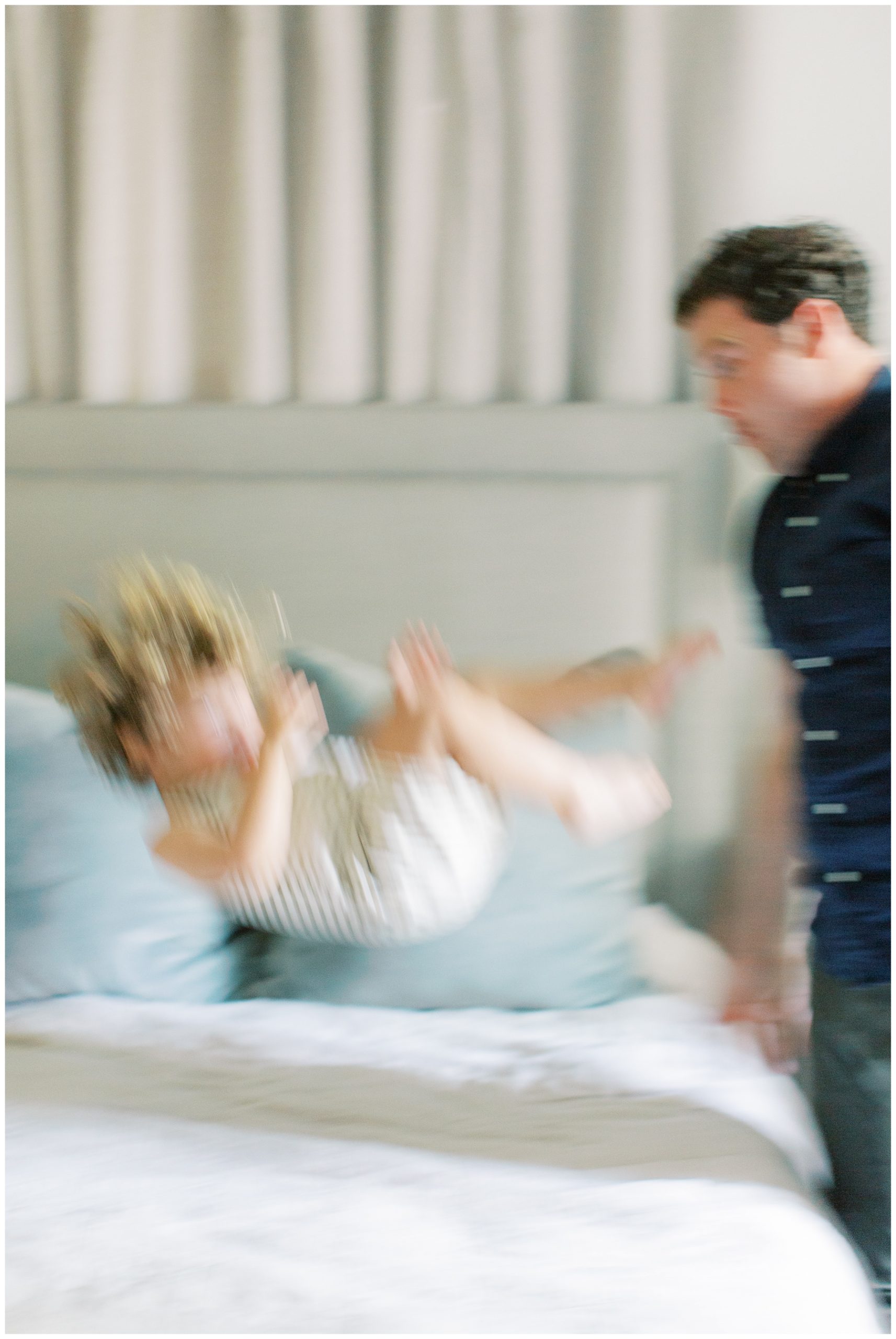 blurred photo of dad playing with toddler on bed during family photos at home 