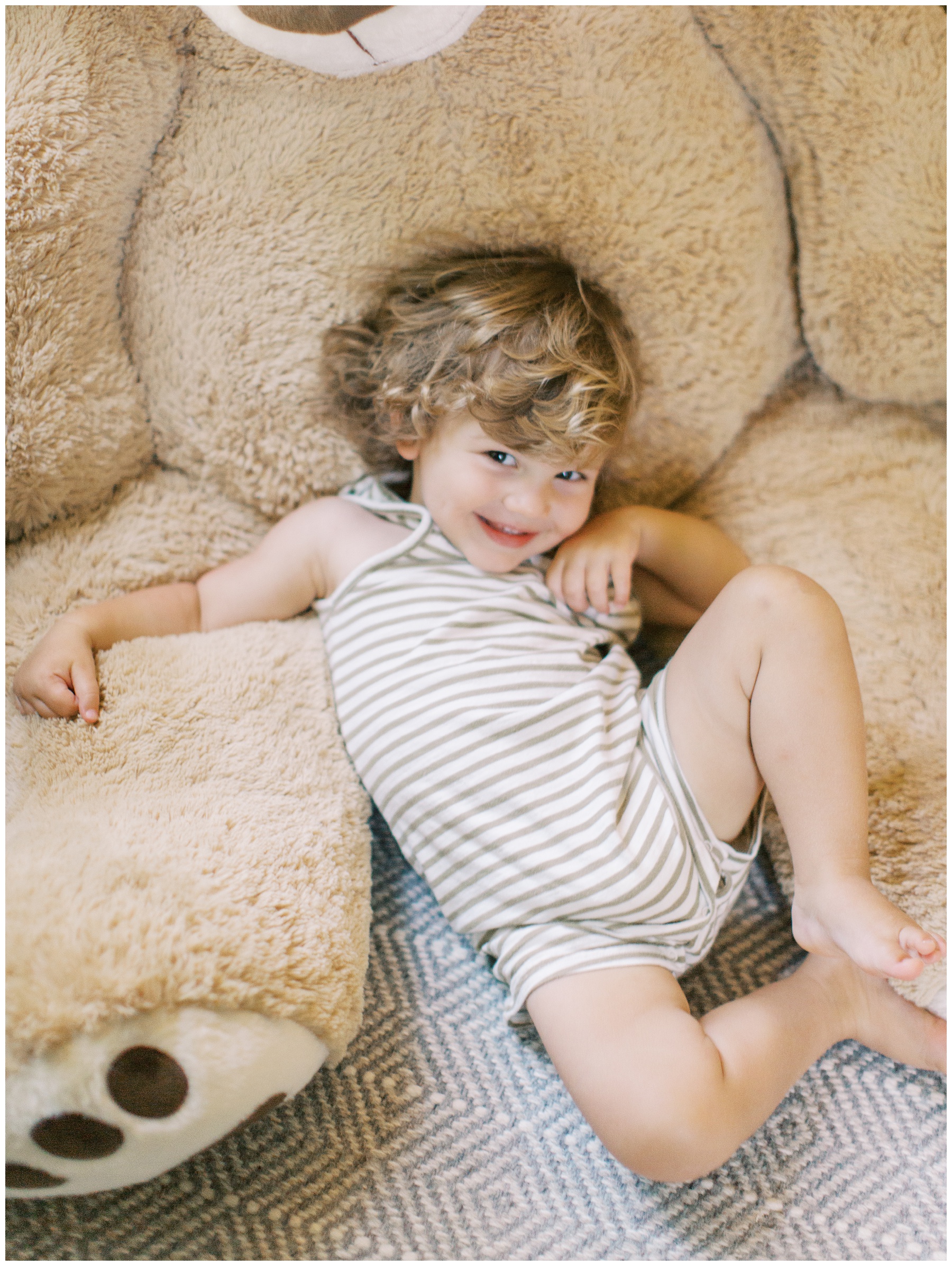 toddler smilies laying against large teddy bear at home 