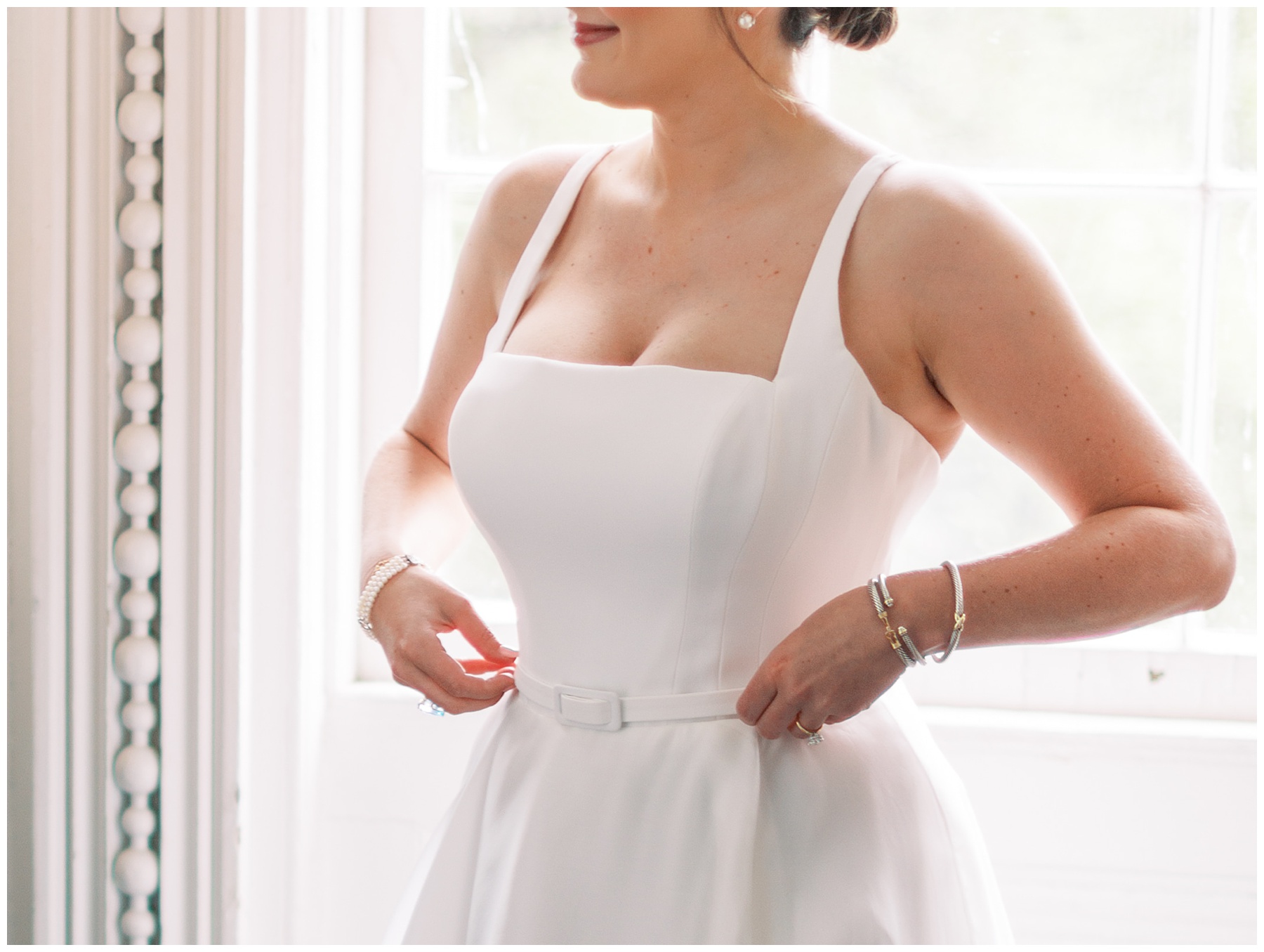 bride adjust white belt on wedding dress in front of window in Charleston SC
