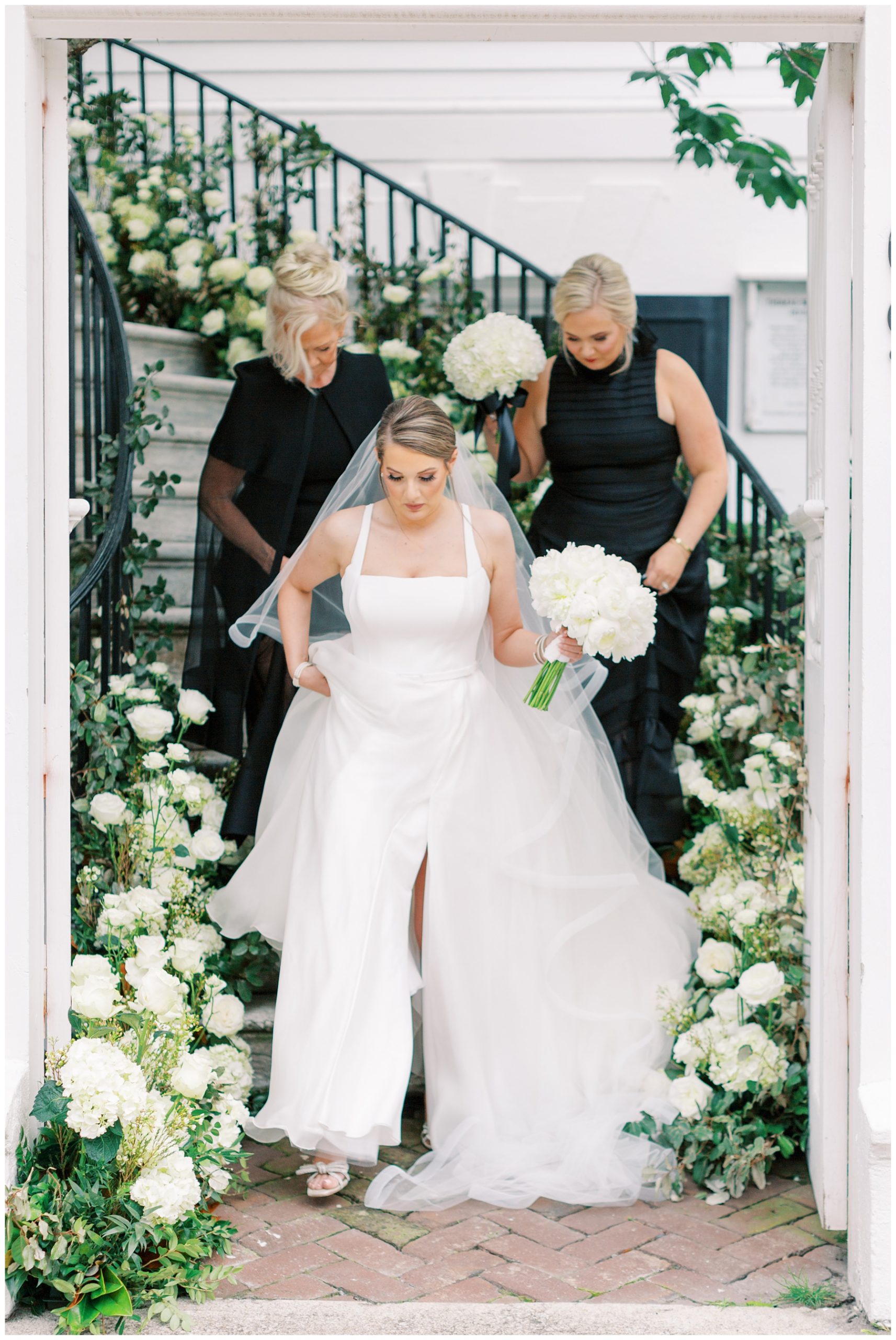 maid of honor and mother in black dresses help bride down steps at the Governor Thomas Bennett House